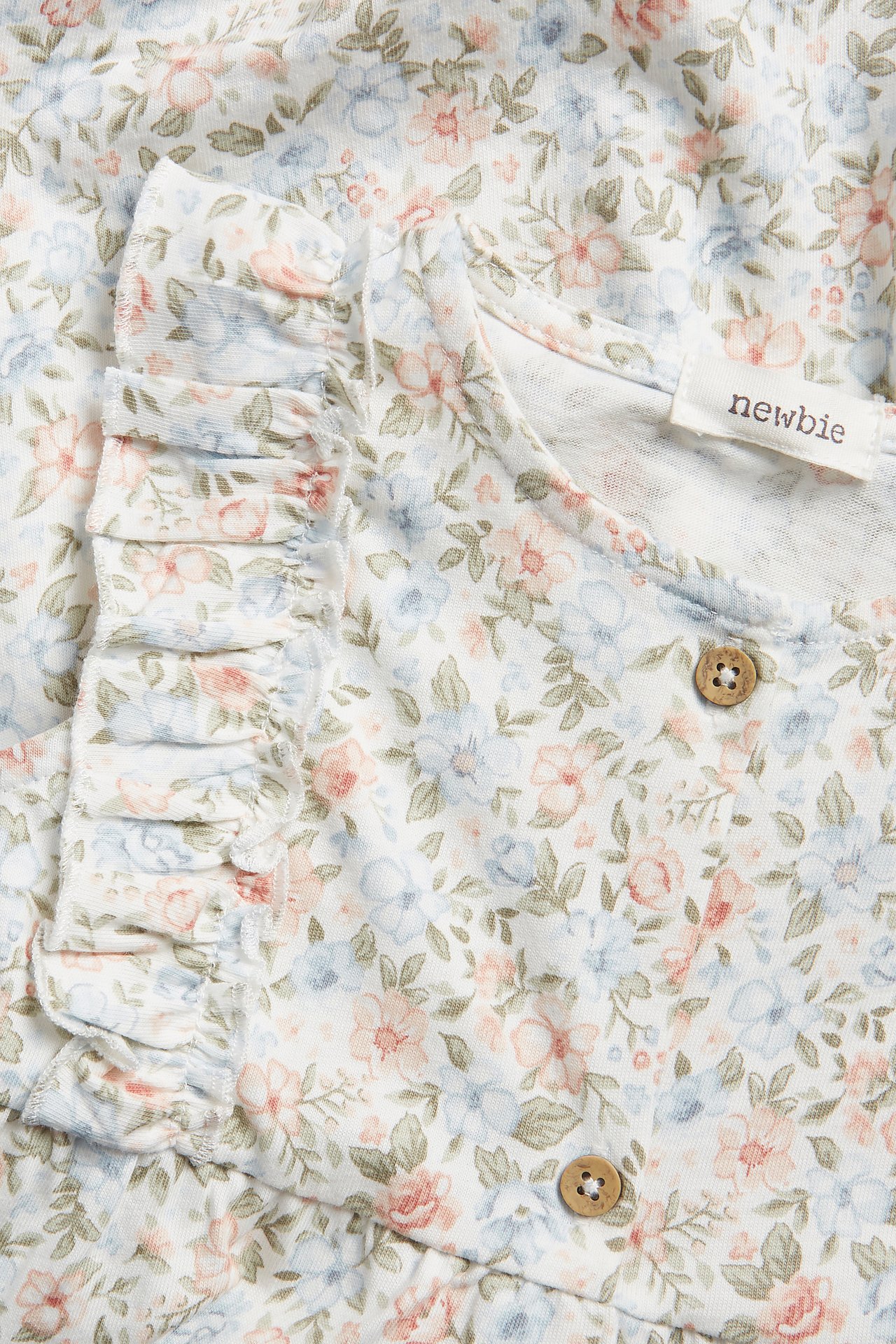 Close-up of an off-white baby playsuit with small floral print, ruffles, and wooden buttons.