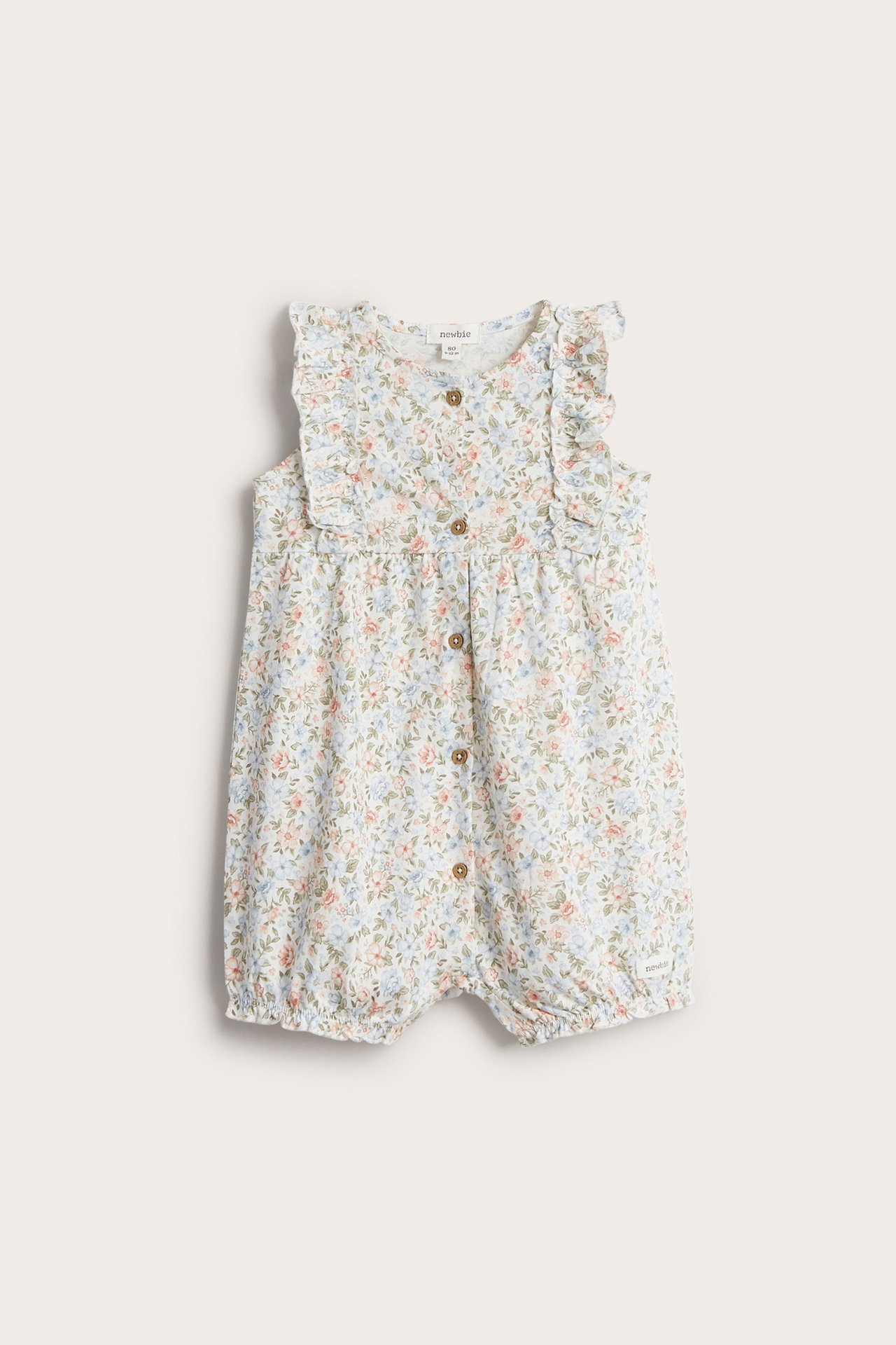 Front view of an off-white baby playsuit with a small floral pattern, ruffles, and front buttons.