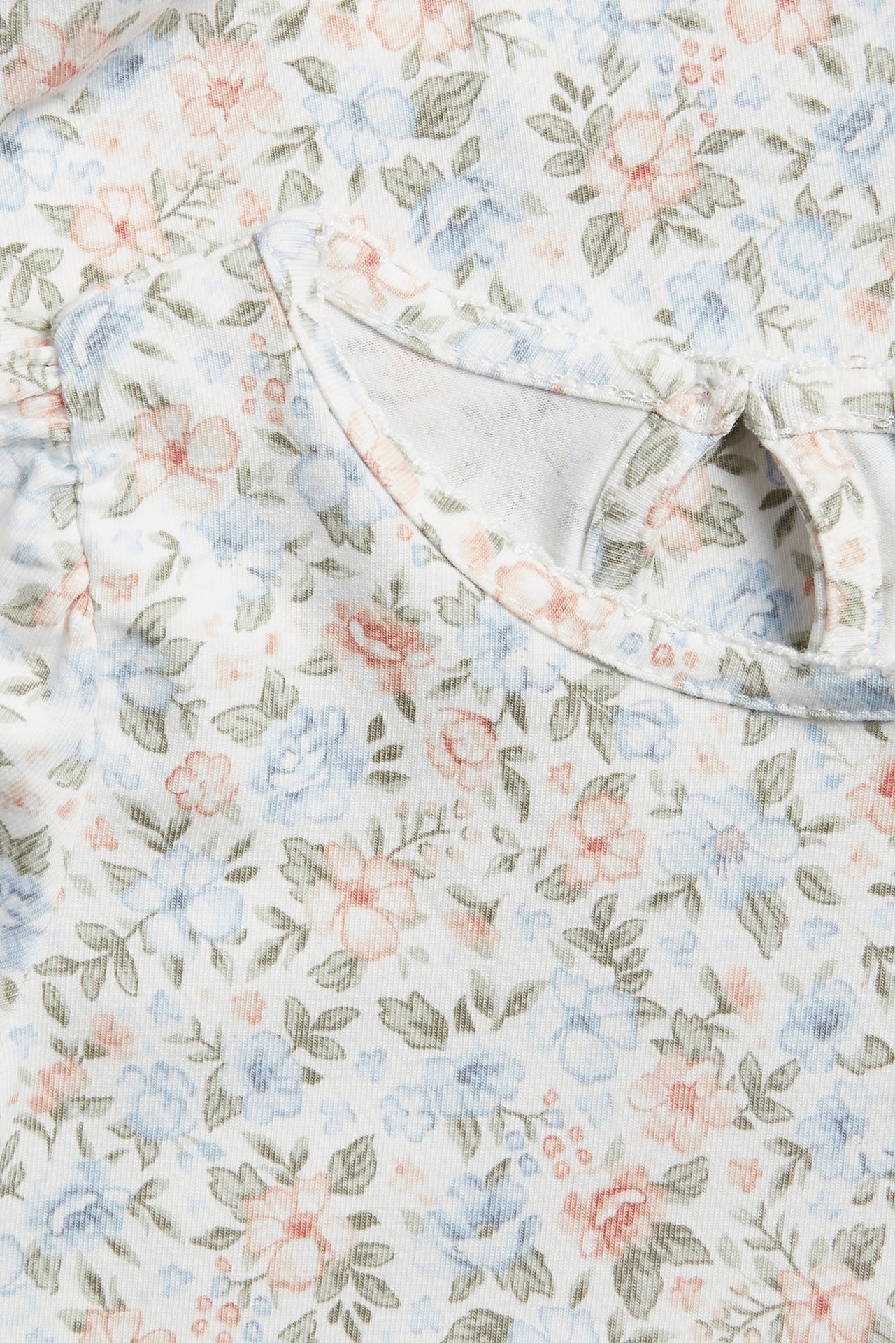 Nahaufnahme eines cremefarbenen Baby-Bodys mit kleinem Blumenmuster, kurzen Puffärmeln und Schlüsselloch-Rückenöffnung.