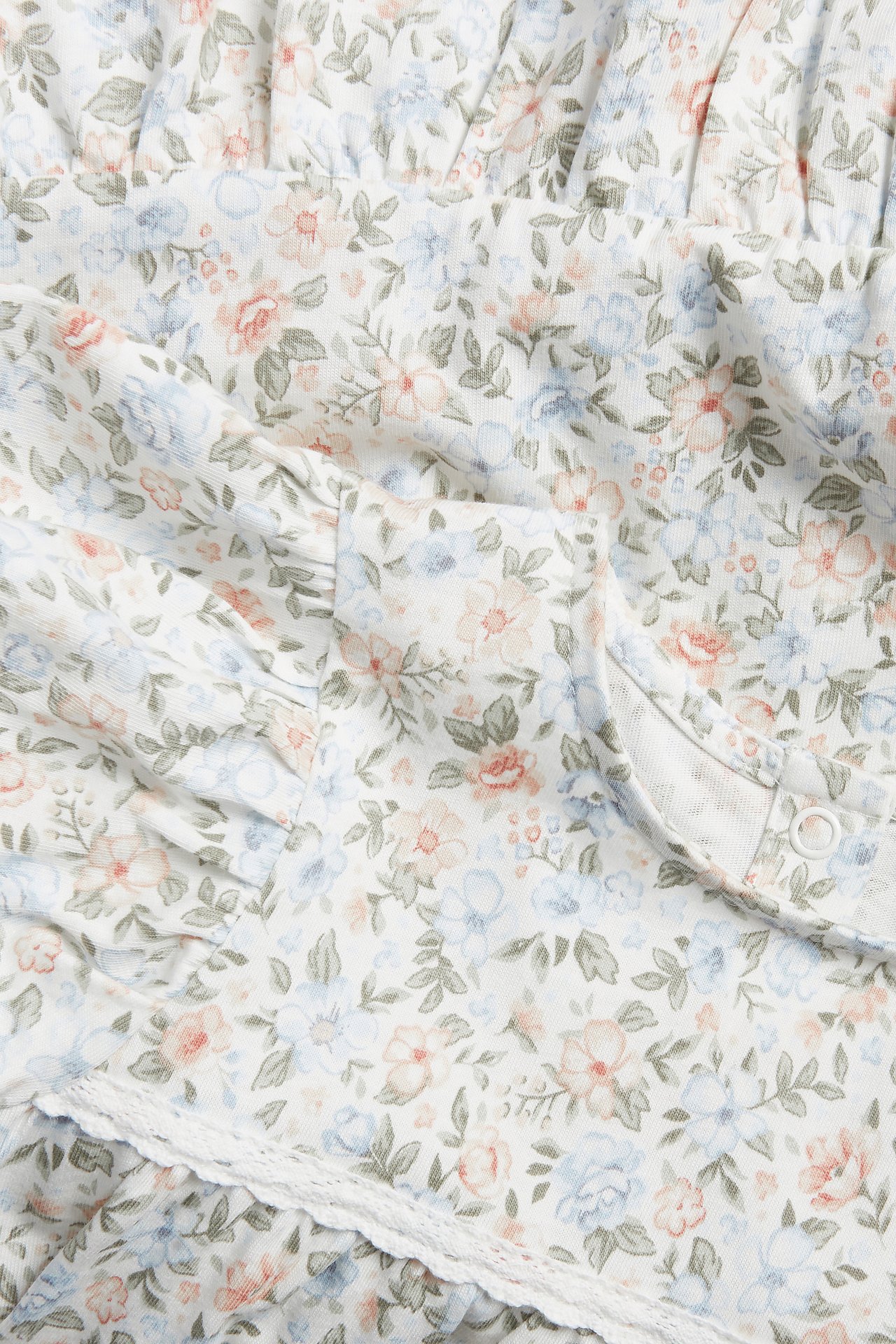Nahaufnahme eines cremefarbenen Baumwoll-Jerseykleides mit kleinem Blumenmuster, Rüschen und weißer Spitze.