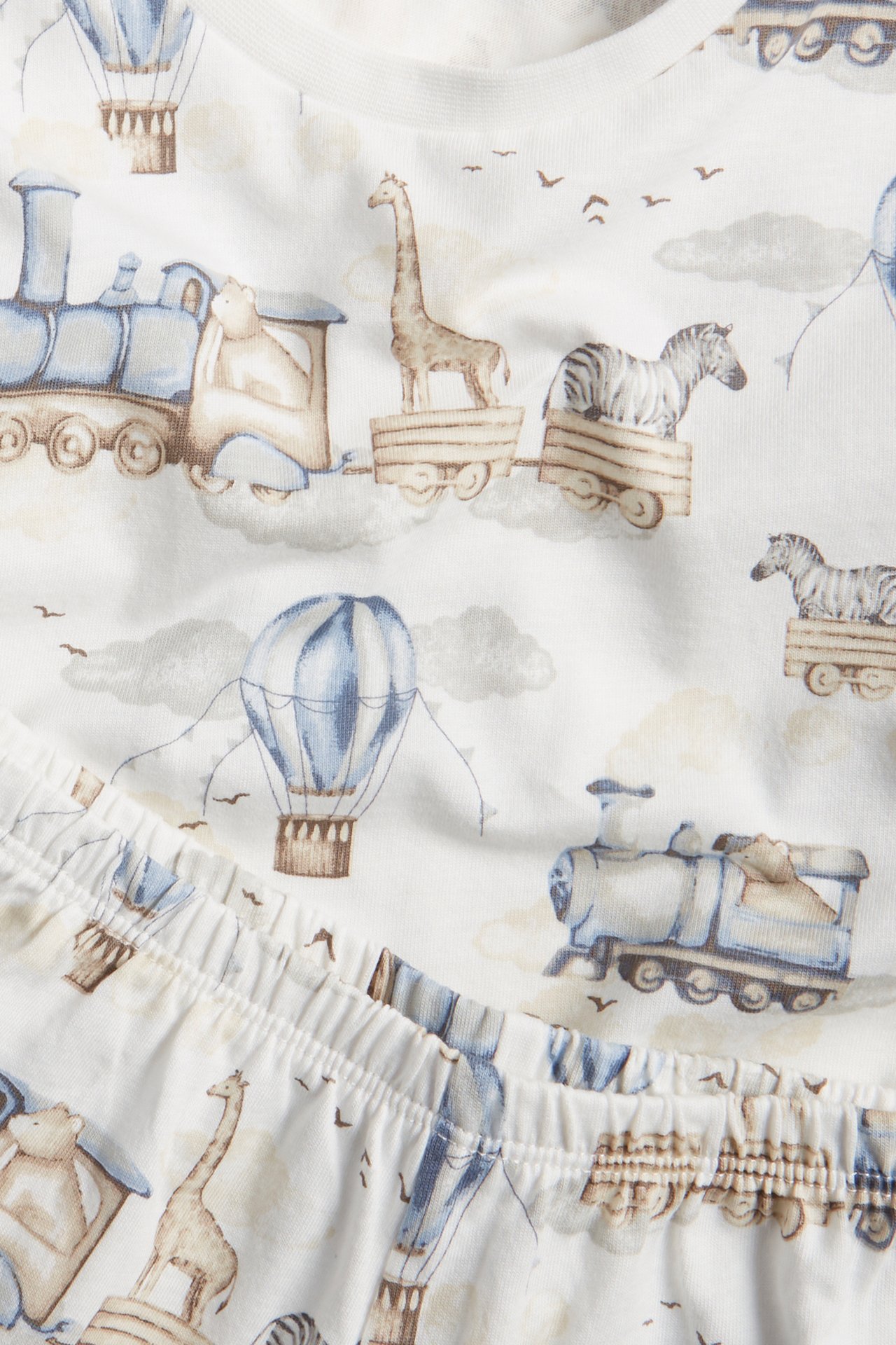 Nahaufnahme: Off-white Baumwoll-Kinderpyjama-Set mit verspieltem Zug-, Heißluftballon- und Tiermuster.