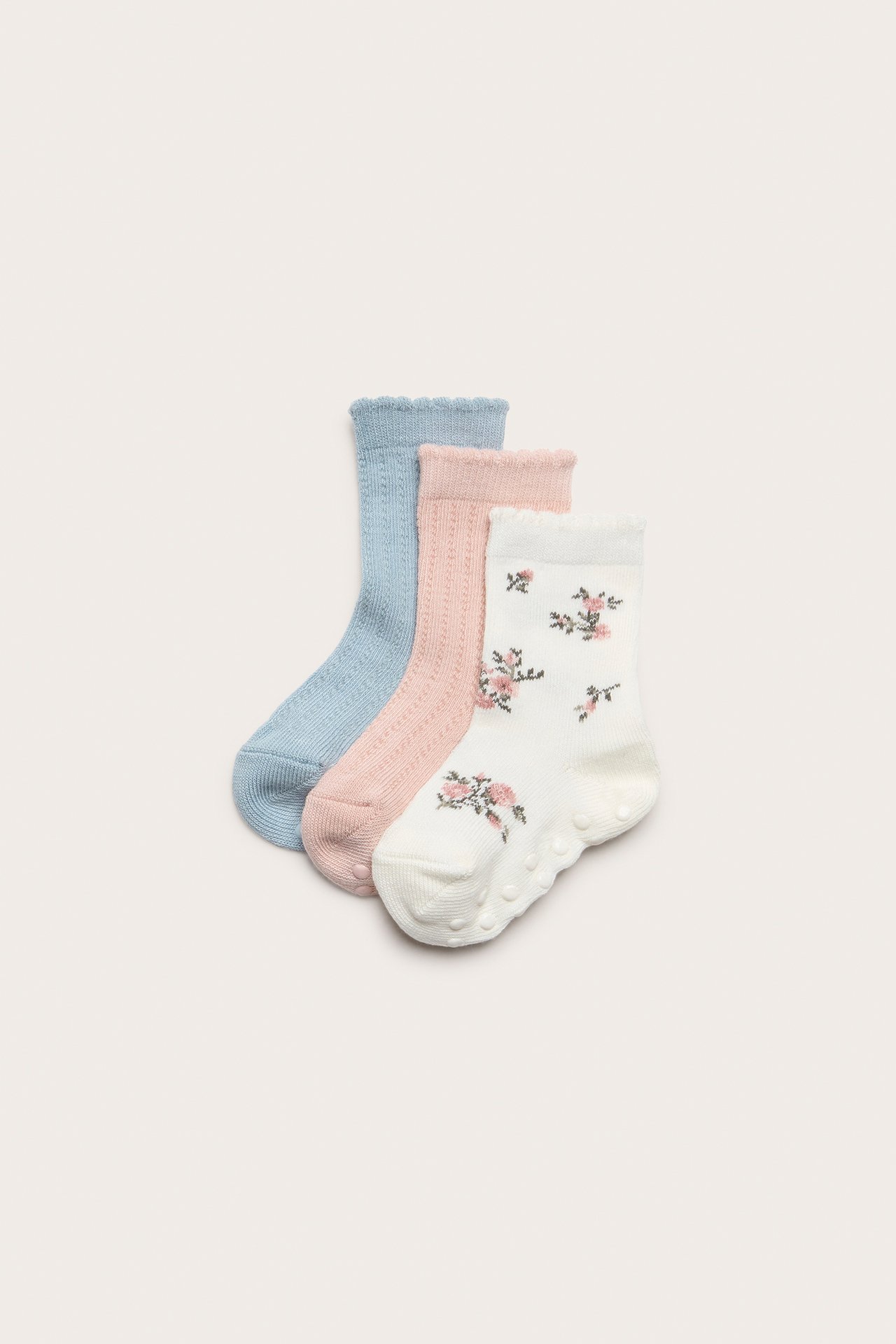 Draufsicht: Drei Babysocken, cremefarben geblümt, hellrosa Spitze, hellblau Spitze, Antirutsch.