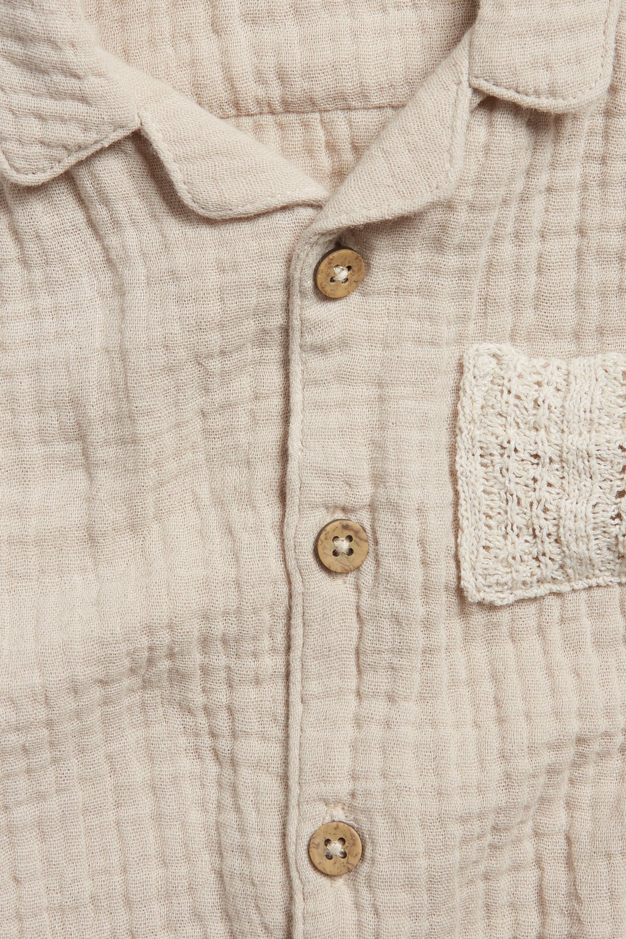 Close-up front view of a beige cotton muslin baby short-sleeved body with wooden buttons and knitted pocket.
