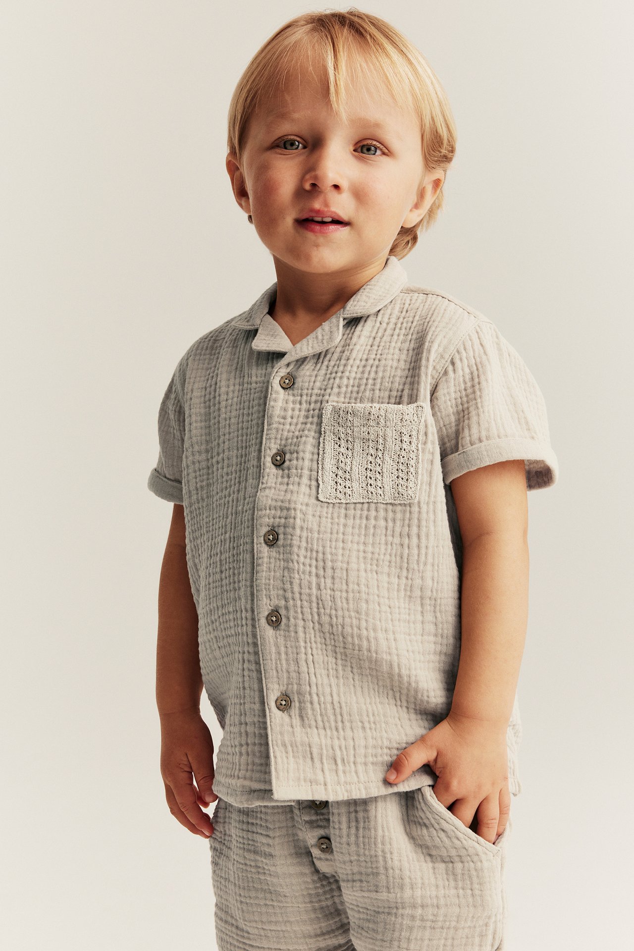 Beige short-sleeved cotton muslin shirt with buttons, textured pocket, and matching shorts on a kid.