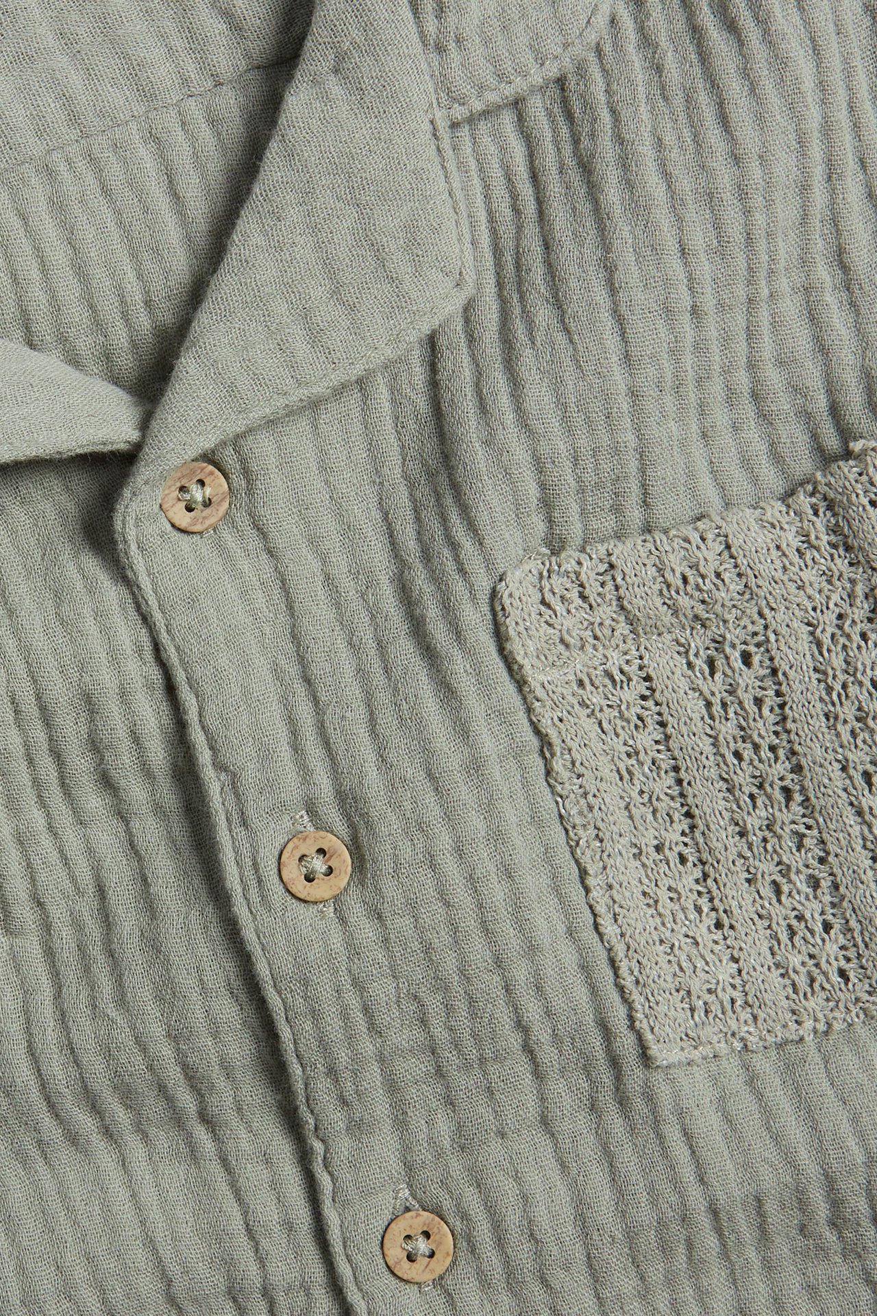Close-up of a green cotton muslin short-sleeved shirt with wooden buttons and a patterned chest pocket.
