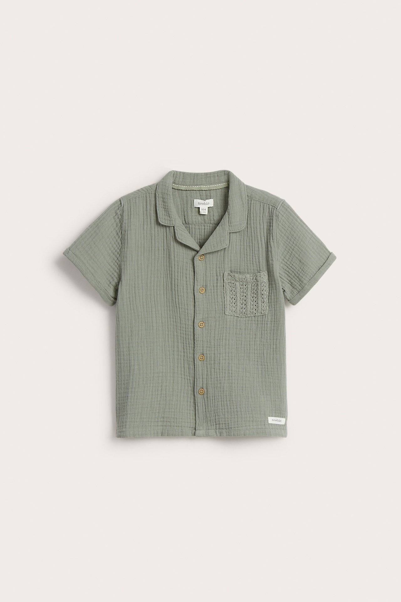 Front view of a kid's green short-sleeved cotton muslin shirt with front buttons and a textured chest pocket.