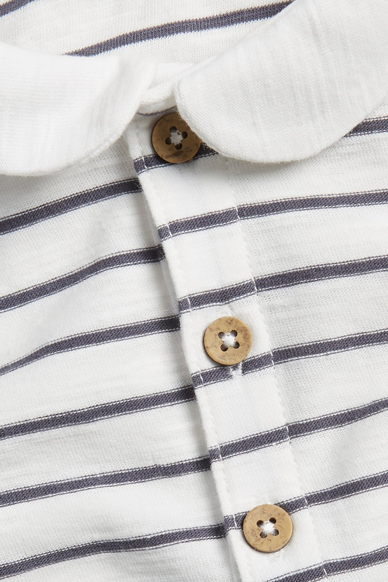 Close-up of a baby's off-white striped cotton bodysuit with a white rounded collar and brown buttons.