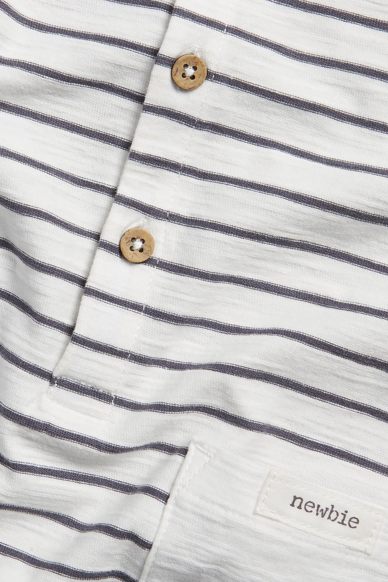 Close-up of an off-white striped slub cotton playsuit with wooden buttons and a patch pocket.