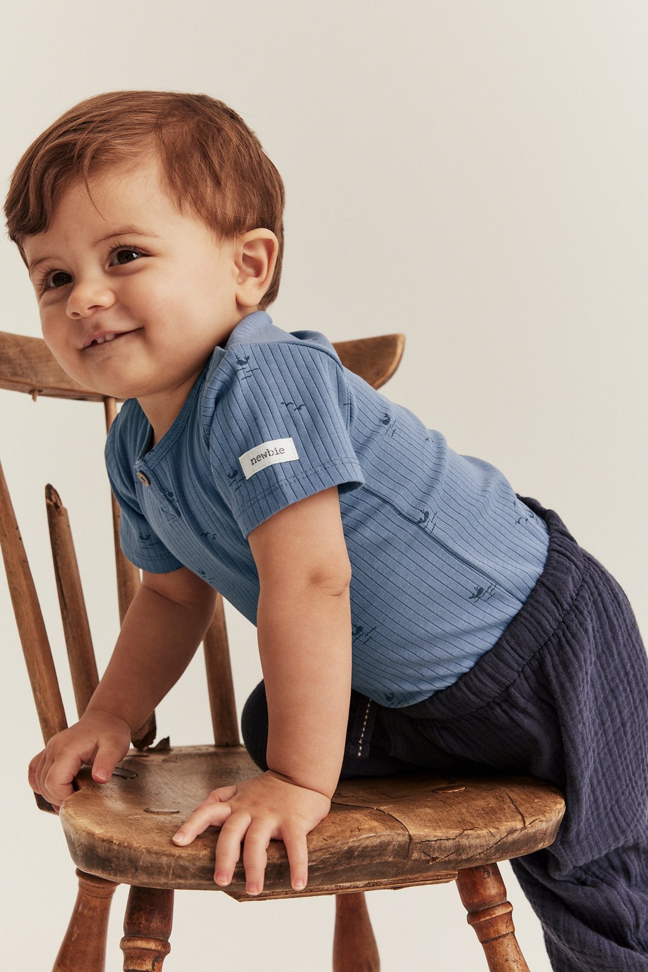 Front view of a baby wearing a blue ribbed short-sleeved bodysuit with a sea pattern and dark blue pants.