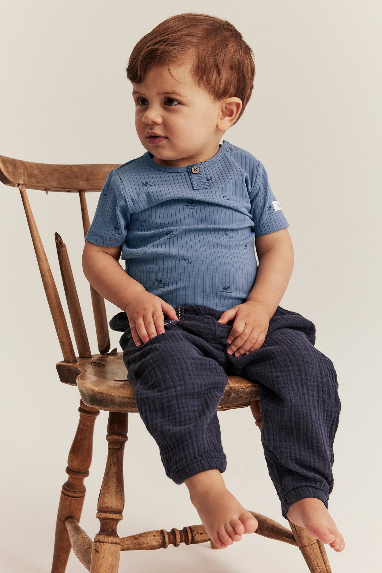 Front view of a baby wearing a blue ribbed short-sleeved body with a sea pattern and dark blue textured pants.