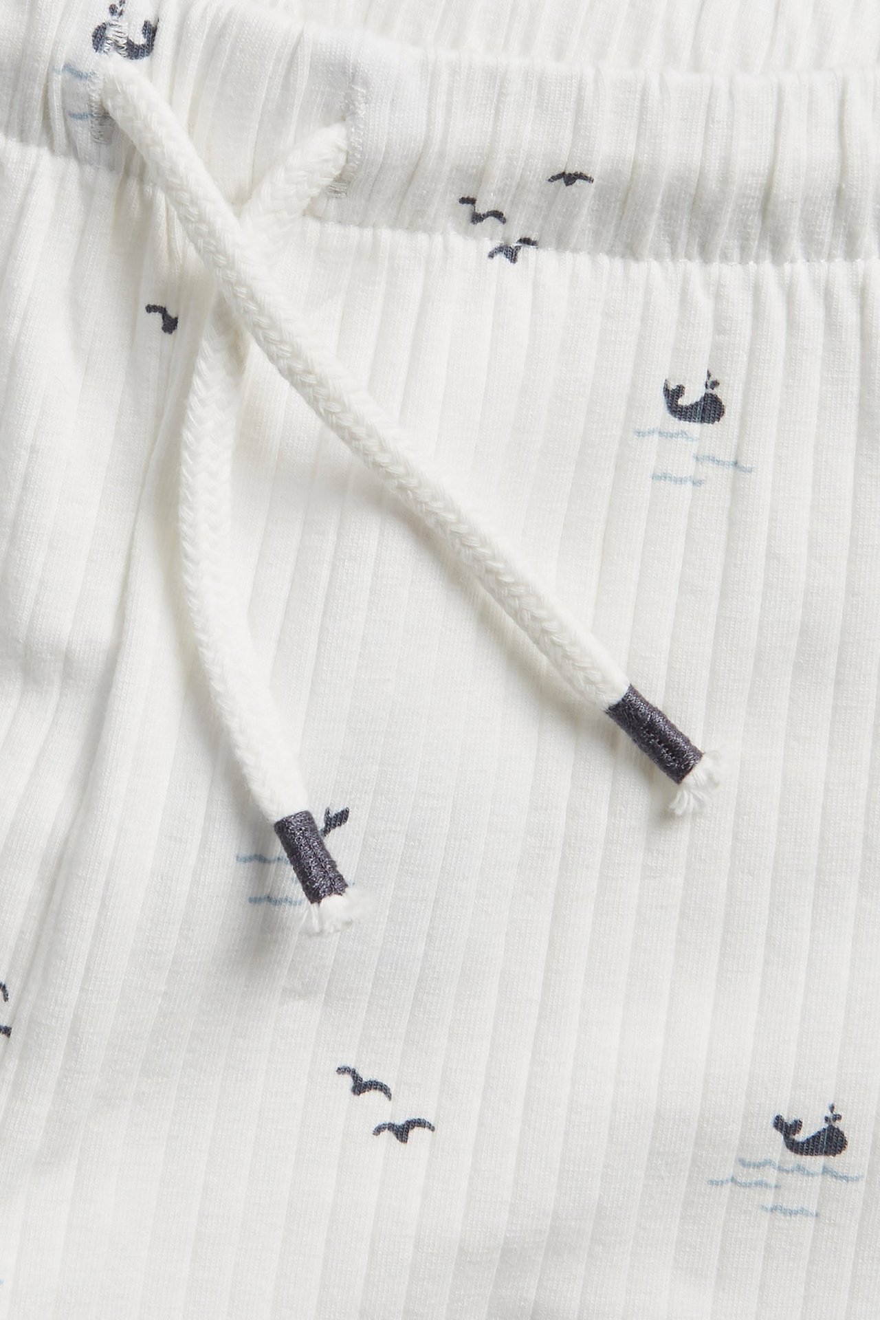 Close-up of off-white ribbed shorts with a sea animal pattern and white drawstring.