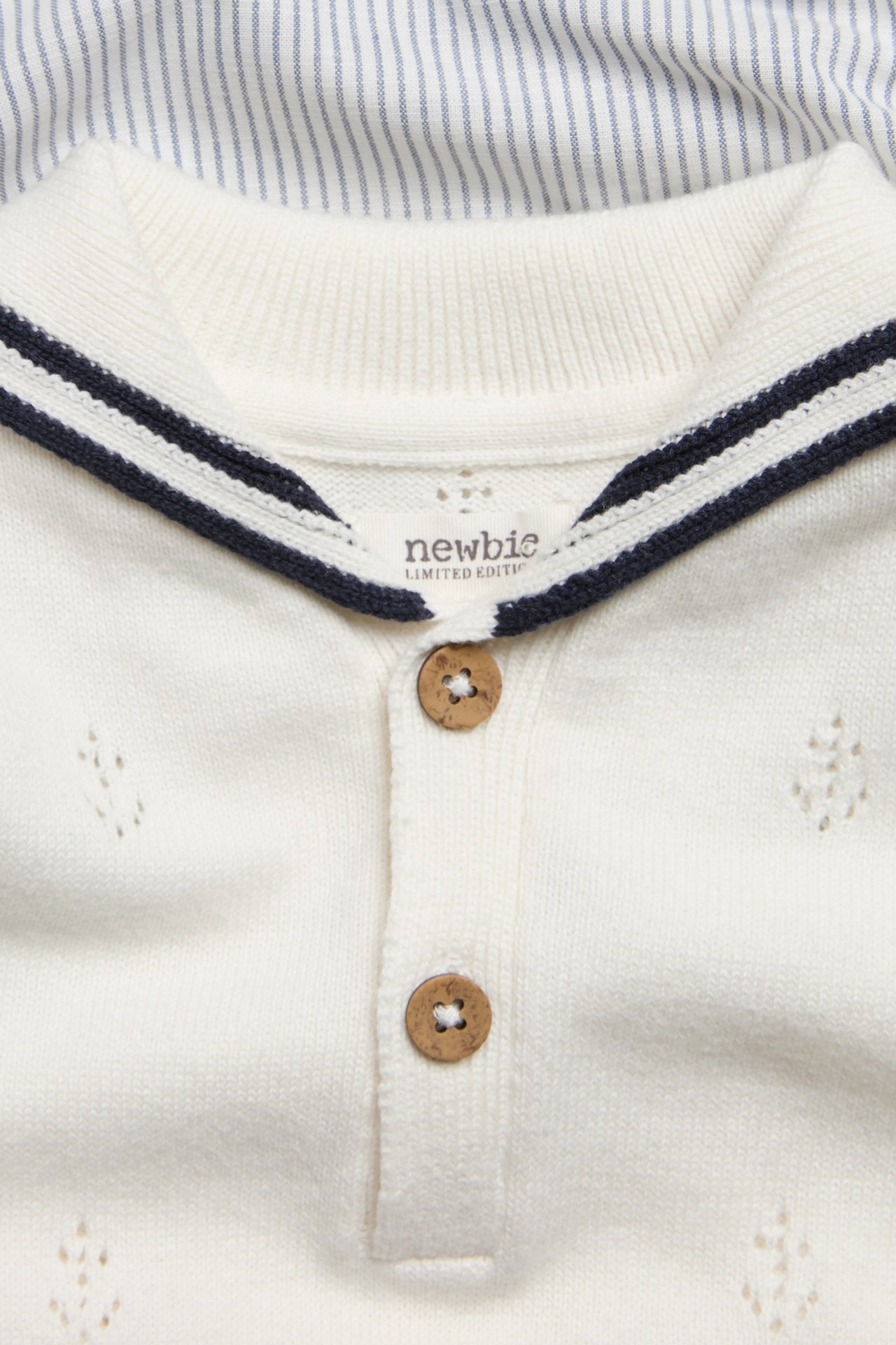 Nahaufnahme: cremeweißer Baby-Playsuit mit Pointelle-Ankern, gestreiftem Matrosenkragen und Holzknöpfen.