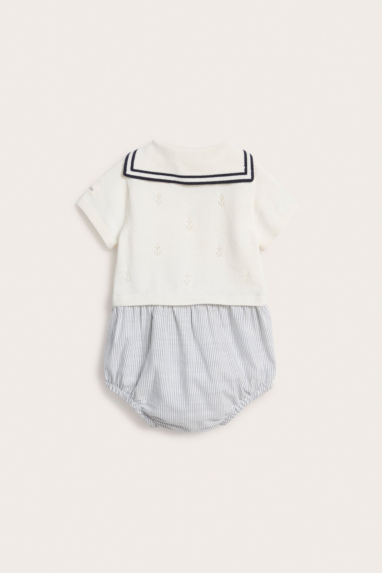 Rückenansicht: Off-white gestrickter Baby-Playsuit mit marineblau gestreiftem Matrosenkragen und hellblau gestreiftem Unterteil.