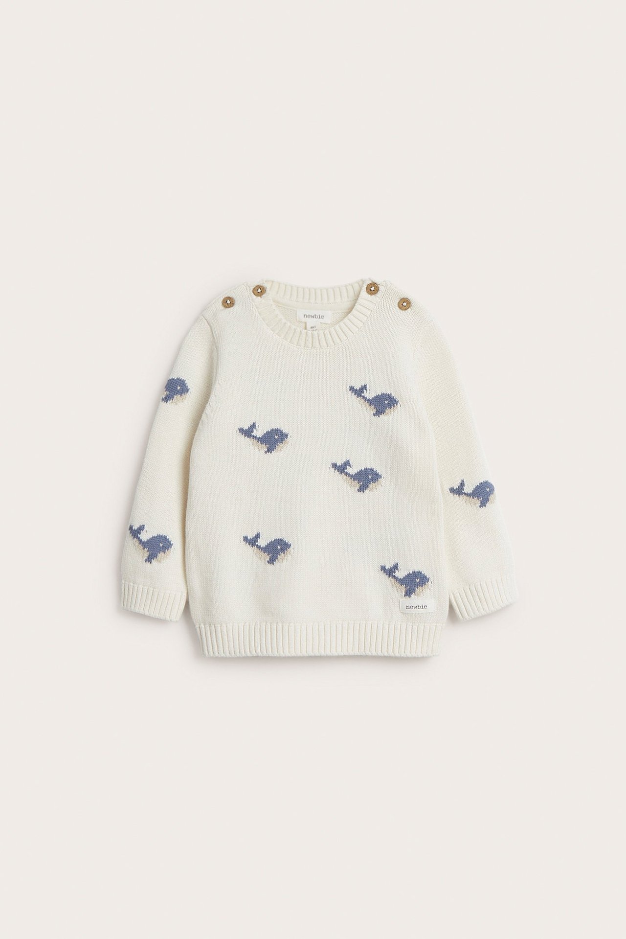 Vorderansicht eines cremefarbenen gestrickten Baby-Baumwollpullovers mit blauem Walmuster und Schulterknöpfen.