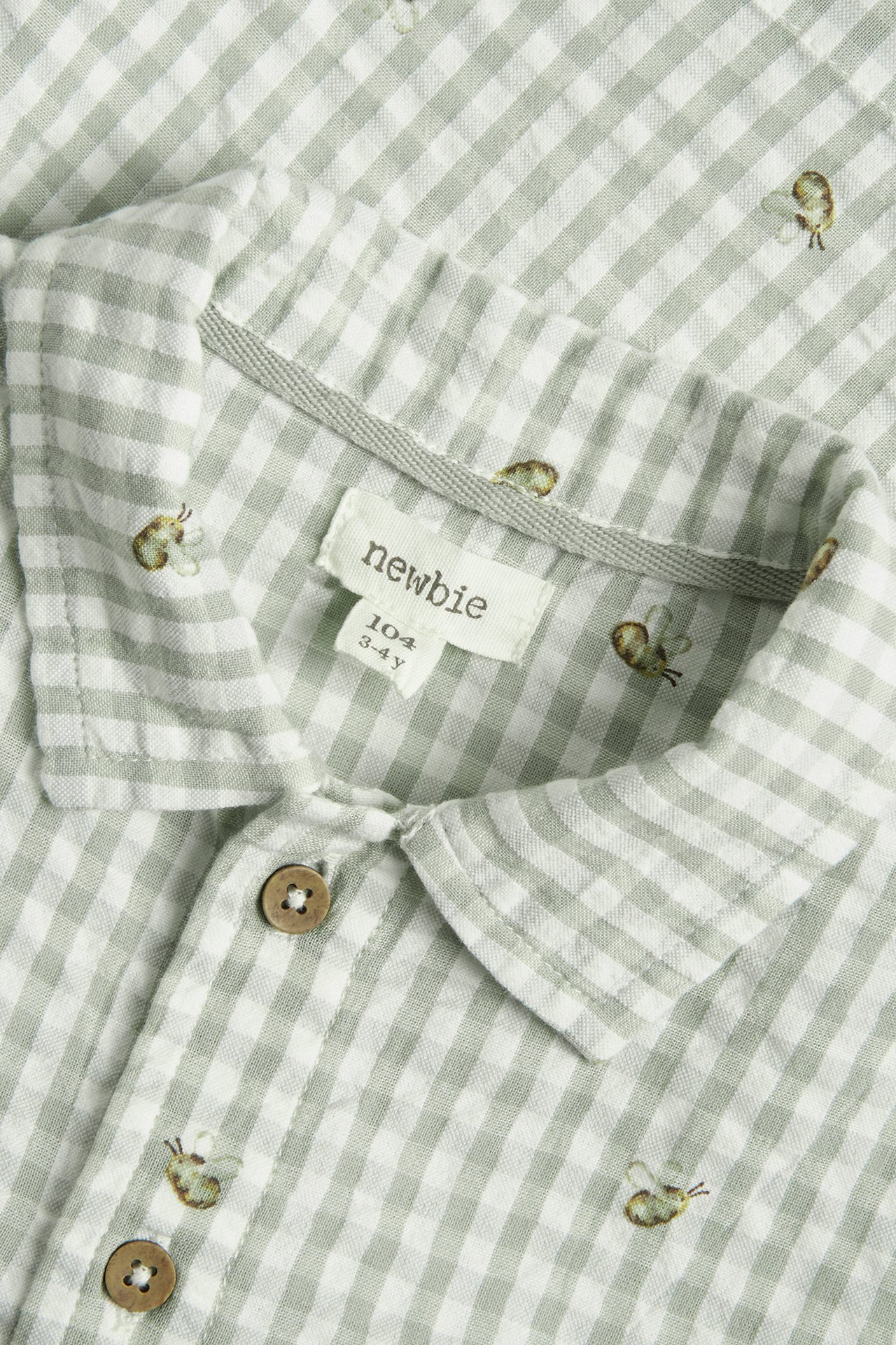 Close-up of a kid's green and white gingham seersucker shirt with small embroidered bees and wooden buttons.