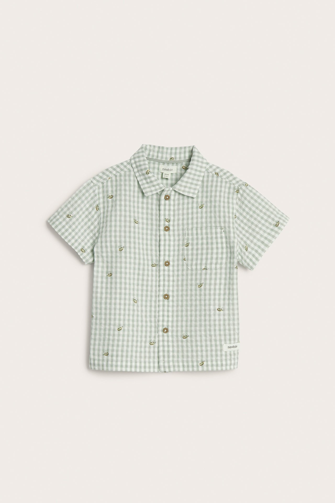Front view: Kid's light green gingham short-sleeved seersucker shirt with small embroidered motifs, front buttons, and chest pocket.