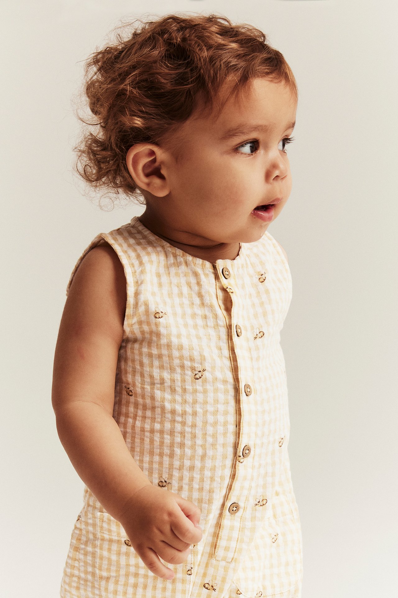 Side view of a baby in a yellow and white checkered seersucker playsuit with small bee pattern.