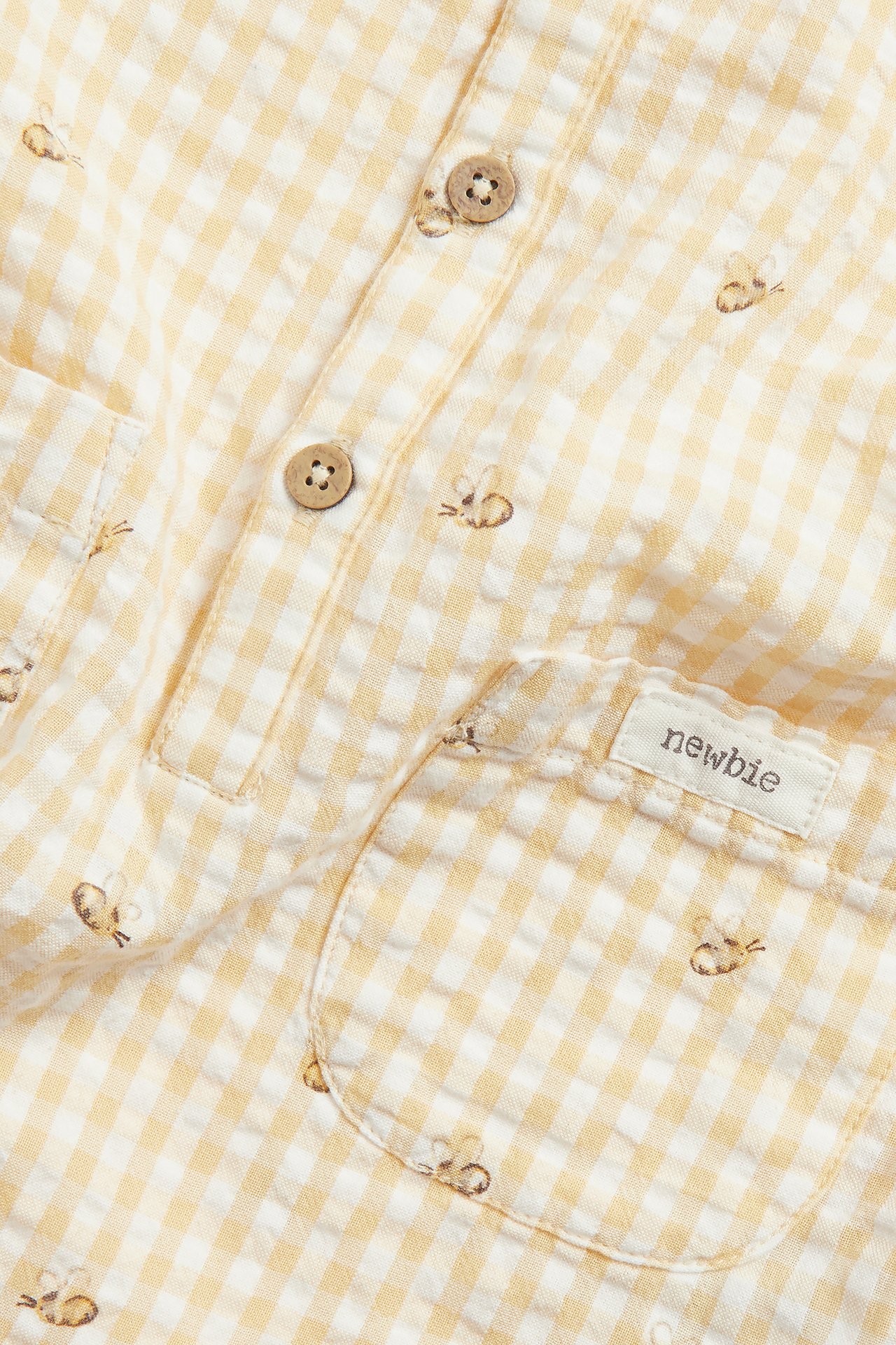 Close-up of a yellow and white gingham seersucker playsuit with bee patterns, wooden buttons, and a pocket.