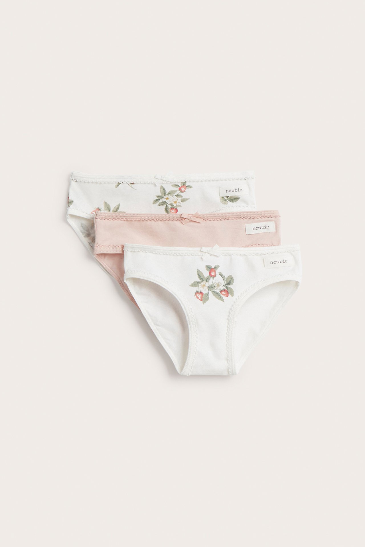 Front view of three kid's cotton panties: off-white with strawberry print, light pink, and off-white floral.