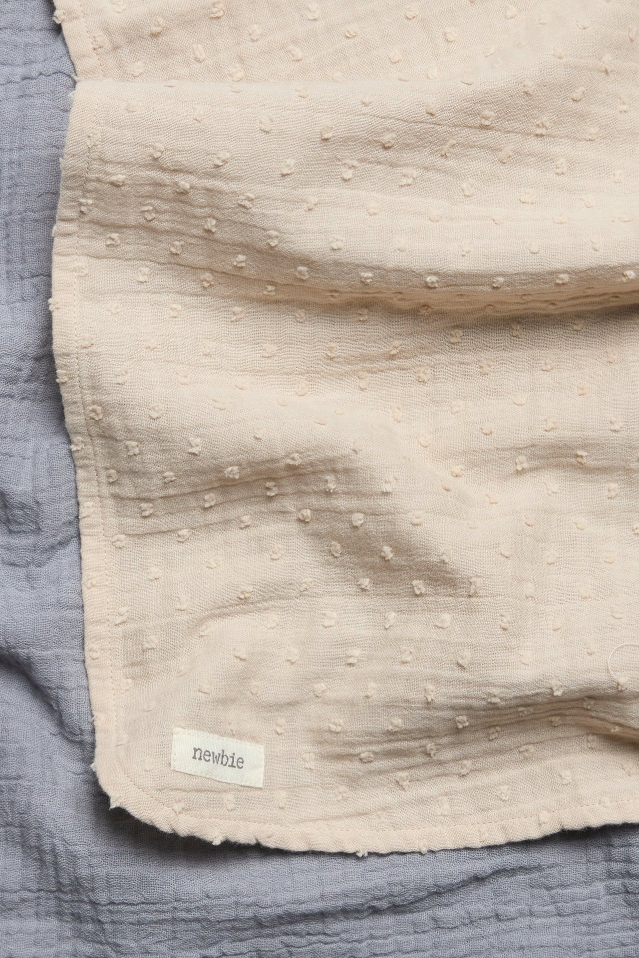 Close-up of a light beige cotton muslin blanket with raised dots, over a plain light blue muslin blanket.