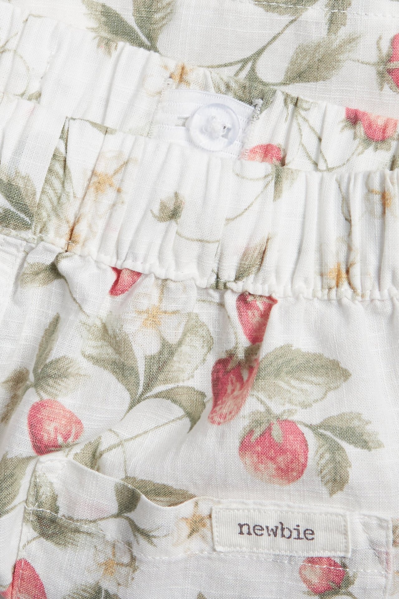 Nahaufnahme von cremeweißen Baumwollshorts mit rotem Erdbeermuster, elastischem Bund und einem transparenten Knopf.