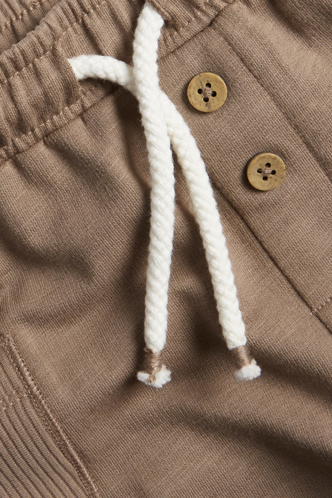 Close-up of brown slub jersey shorts with an elastic waist, white drawstring, and decorative buttons.