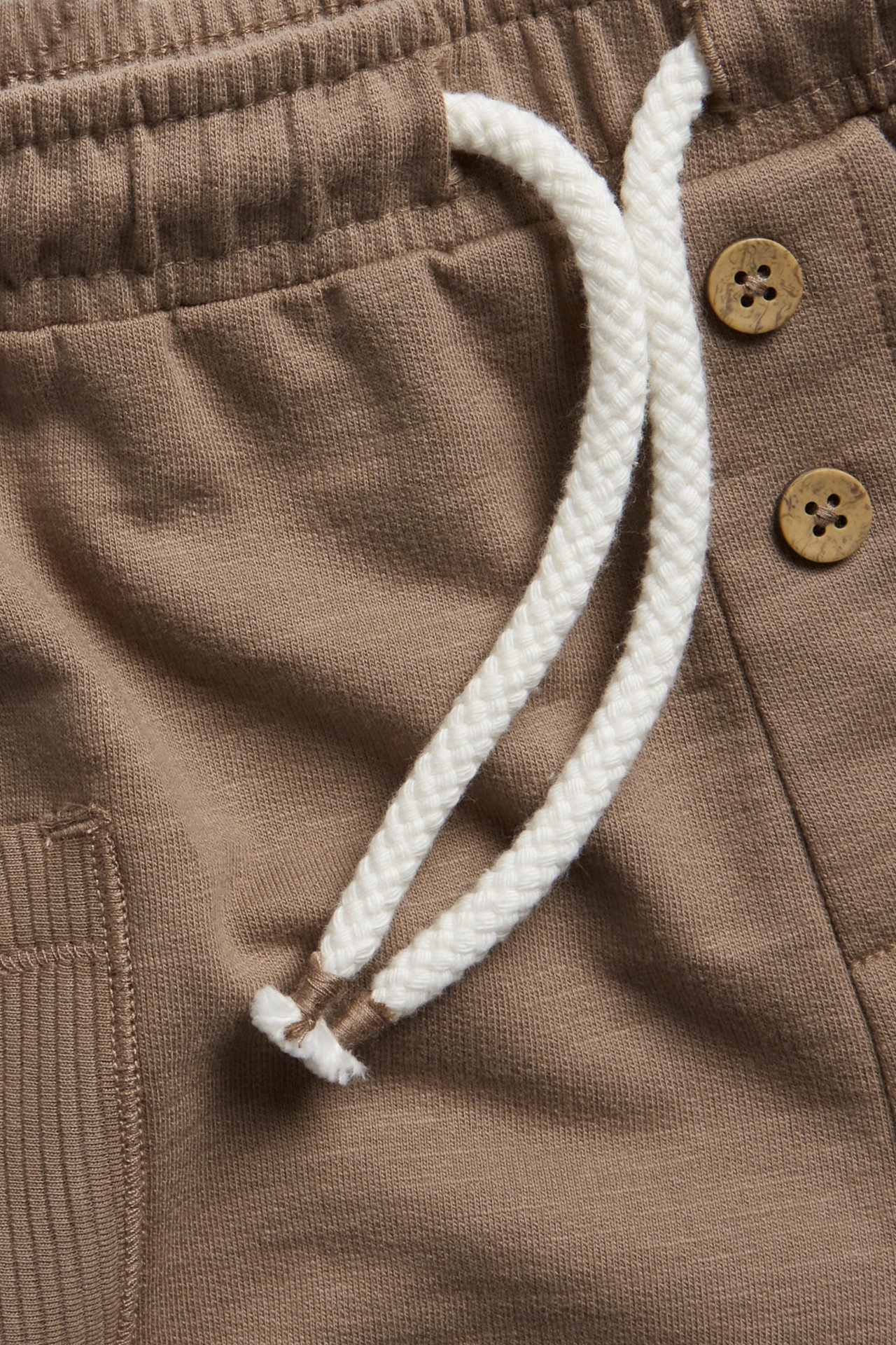 Nahaufnahme brauner Slub-Jersey-Shorts mit elastischem Bund, weißem Kordelzug und dekorativen Holzknöpfen.