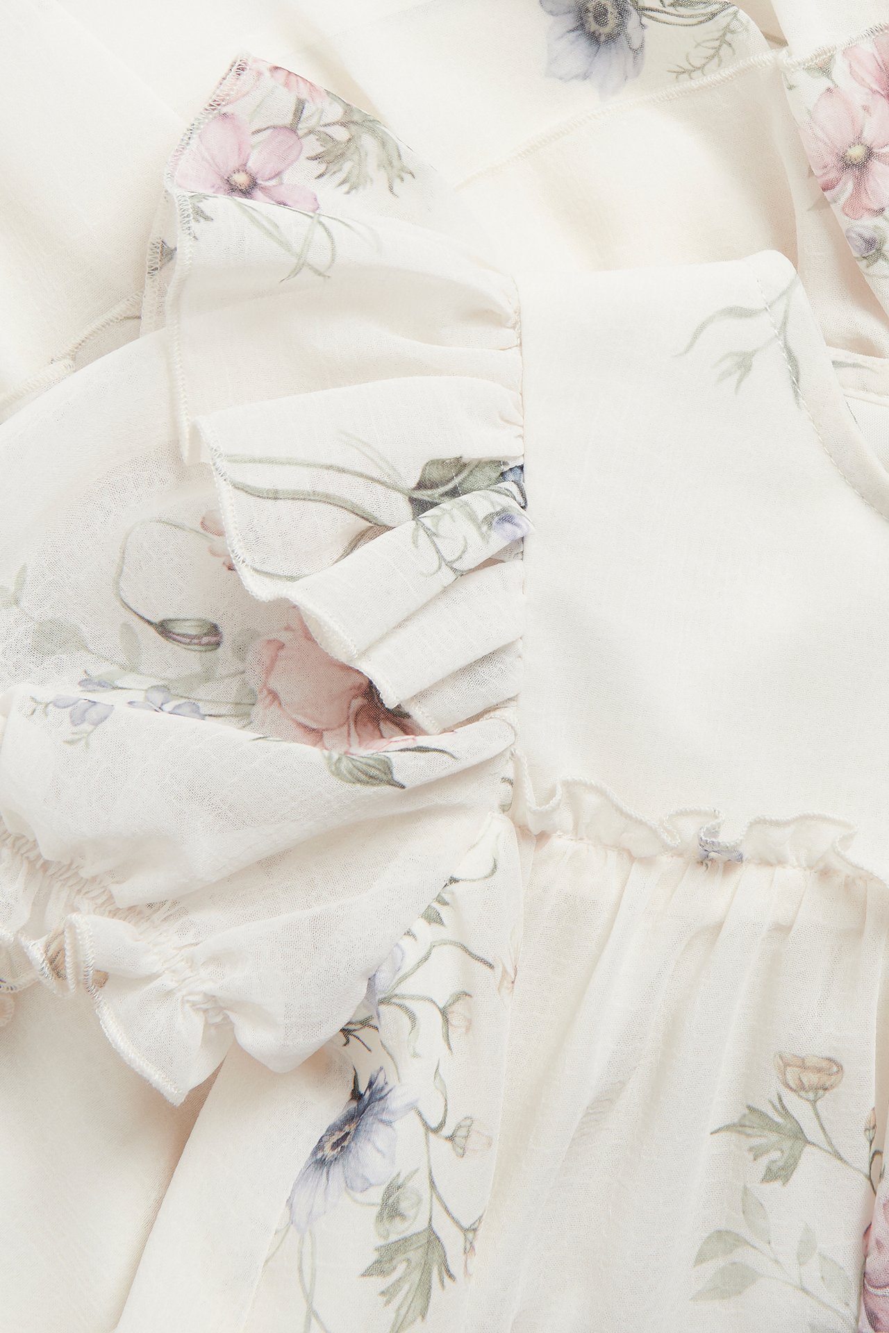 Close-up of an off-white floral chiffon dress with ruffles and babylock seams.