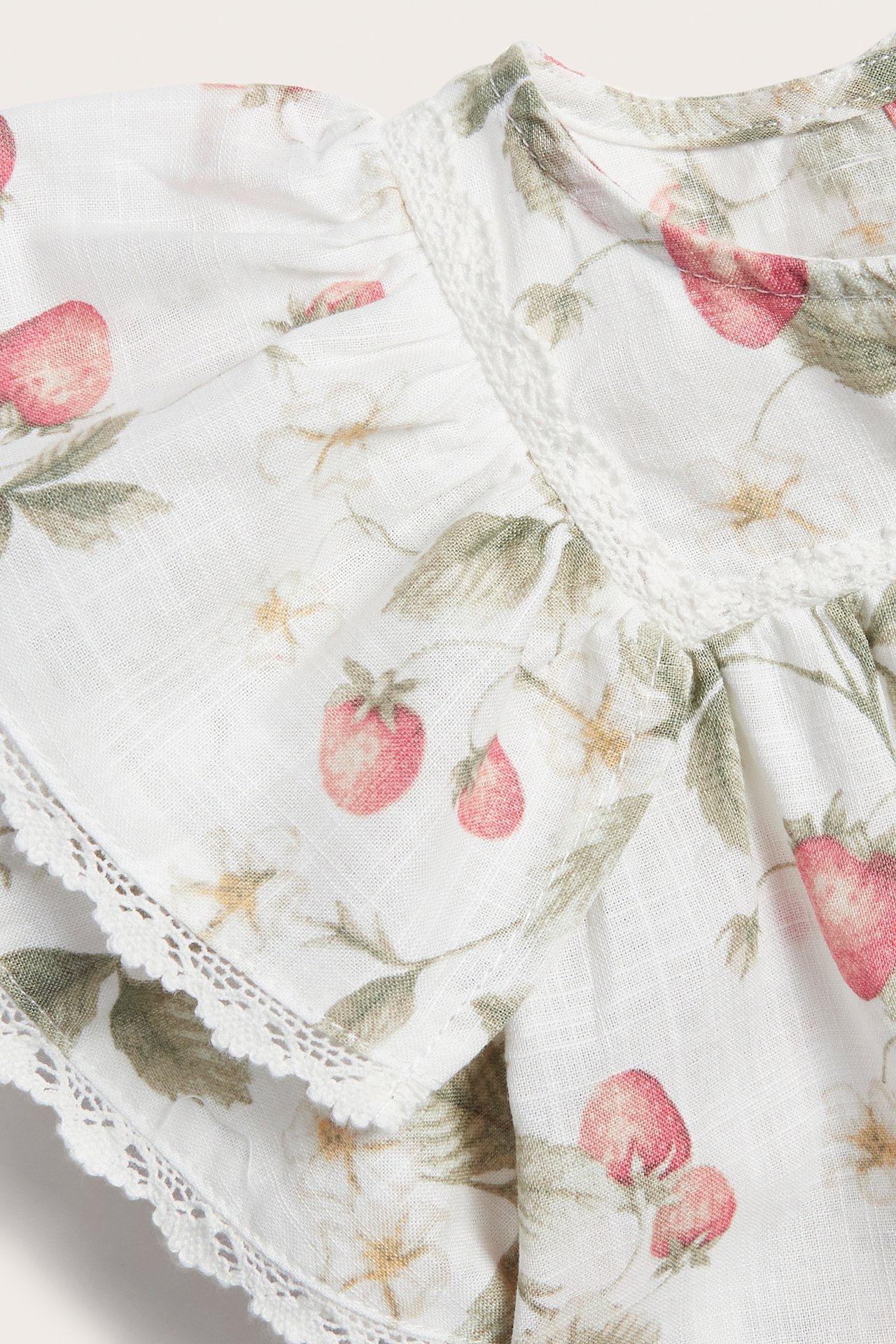 Close-up of an off-white cotton dress with a strawberry pattern, butterfly sleeves, ruffles, and lace edges.