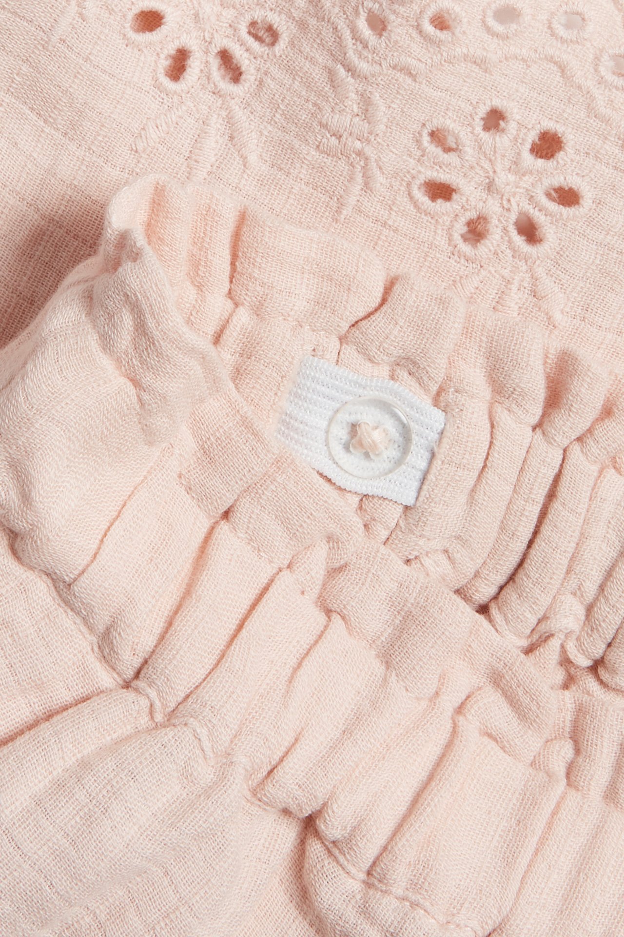 Nahaufnahme von hellrosa gewebten Baumwollshorts mit gesticktem Lochmuster und verstellbarem Gummibund mit Knopf.