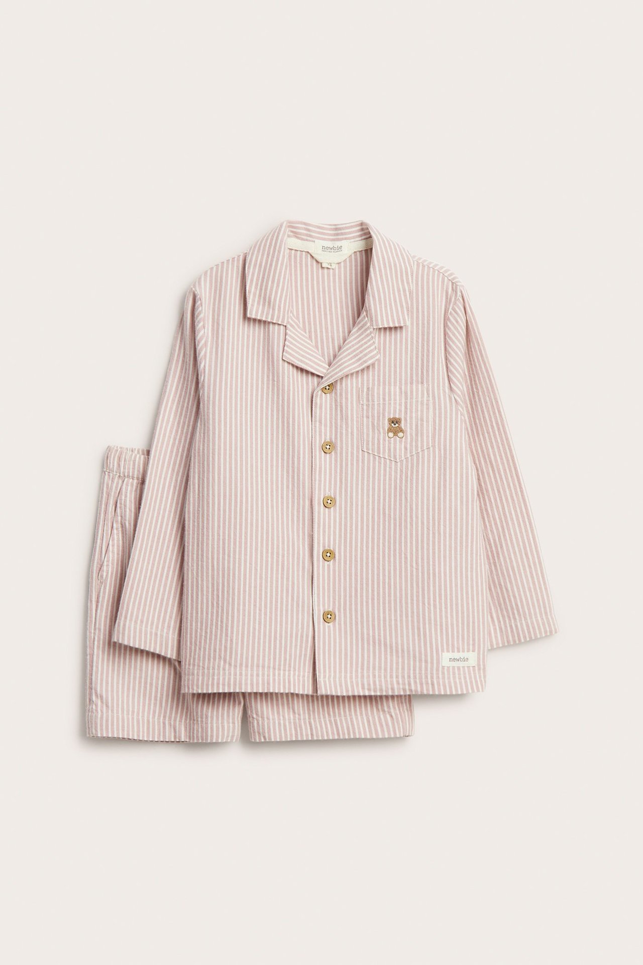 Vorderansicht eines gestreiften Kinder-Pyjama-Sets in Rosa und Weiß: Langarmshirt mit Teddybär und Shorts.