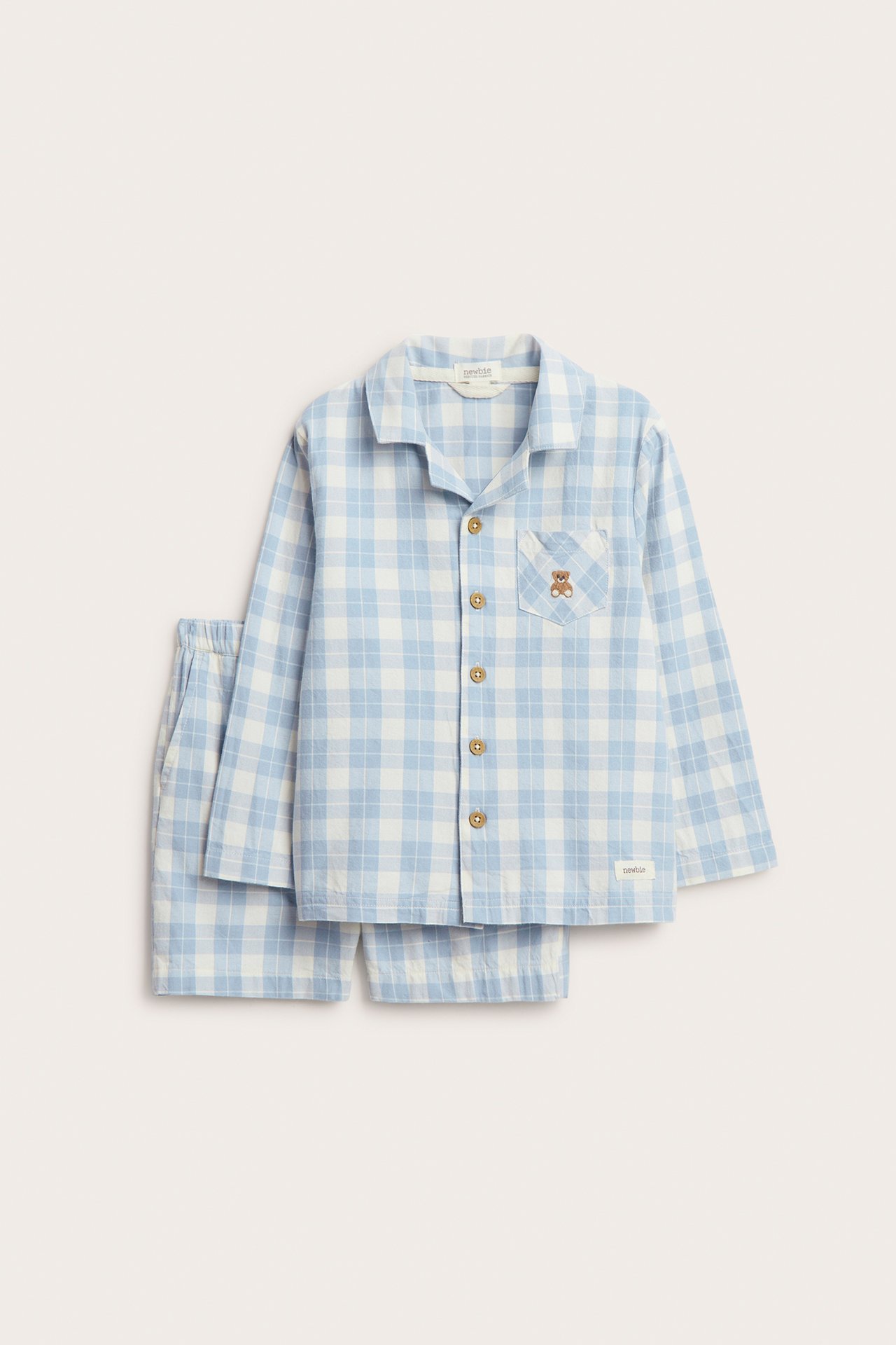 Vorderansicht eines blau-weiß karierten Kinder-Pyjamas aus Baumwolle: Langarmshirt mit Teddy-Stickerei, Shorts.