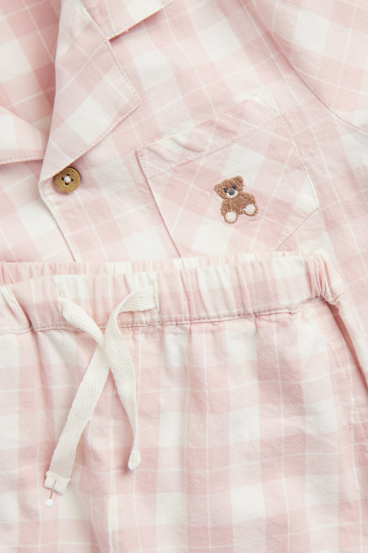 Nahaufnahme eines rosa-weiß karierten Kinder-Baumwollpyjama-Sets mit bestickter Tasche und Shorts mit Kordelzug.