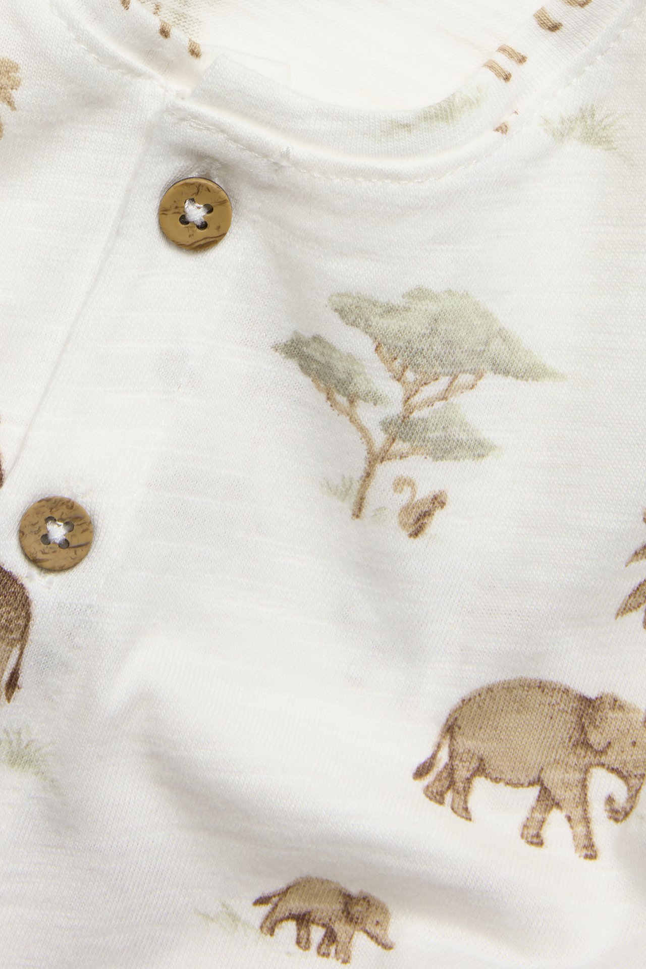 Close-up of an off-white baby playsuit in slub cotton with a brown elephant pattern and brown buttons.