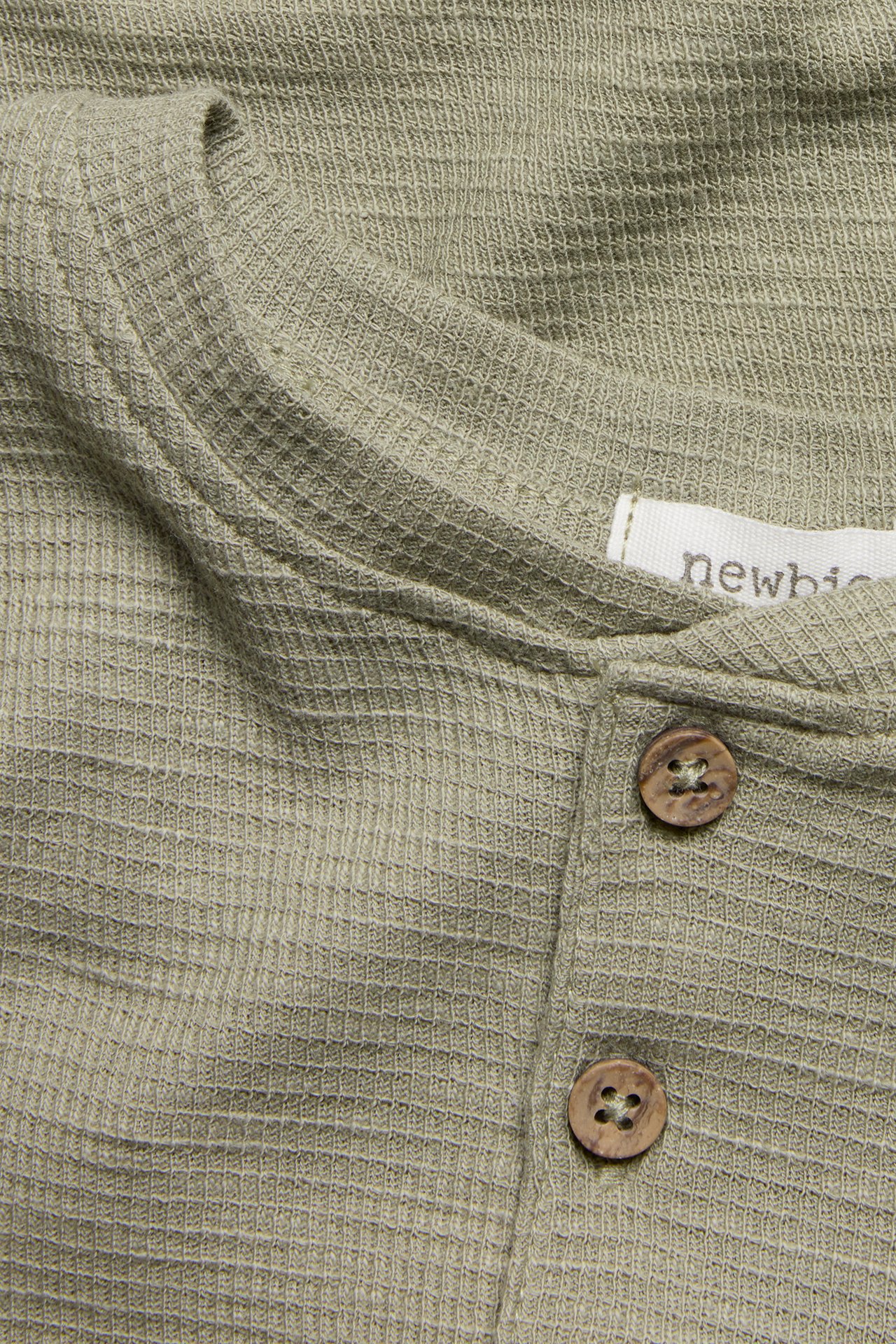 Close-up of a dark green waffle-knit cotton long-sleeved top with two brown wooden buttons.