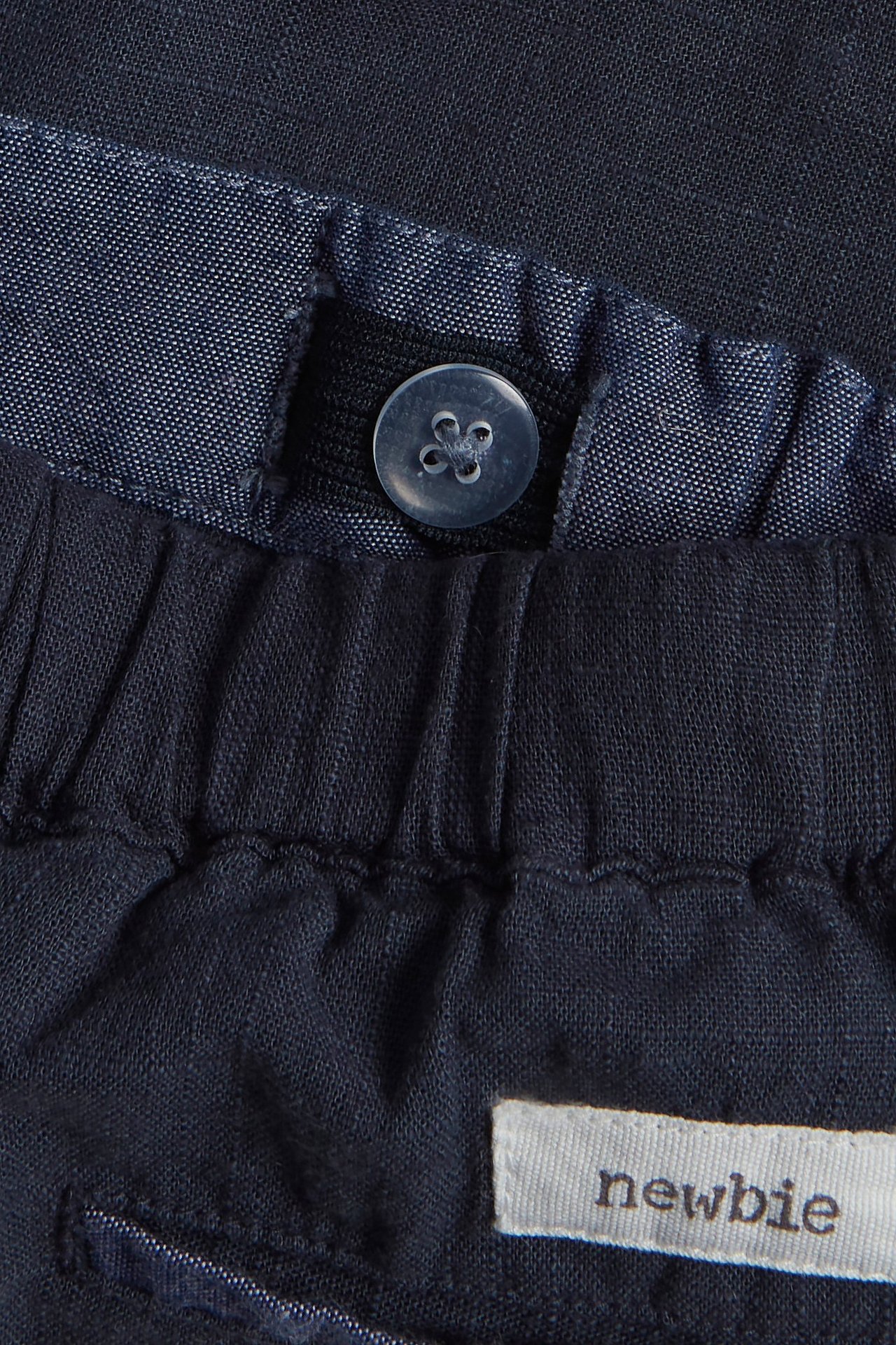 Close-up of dark blue woven shorts with an elastic waistband, a button, and chambray detail.