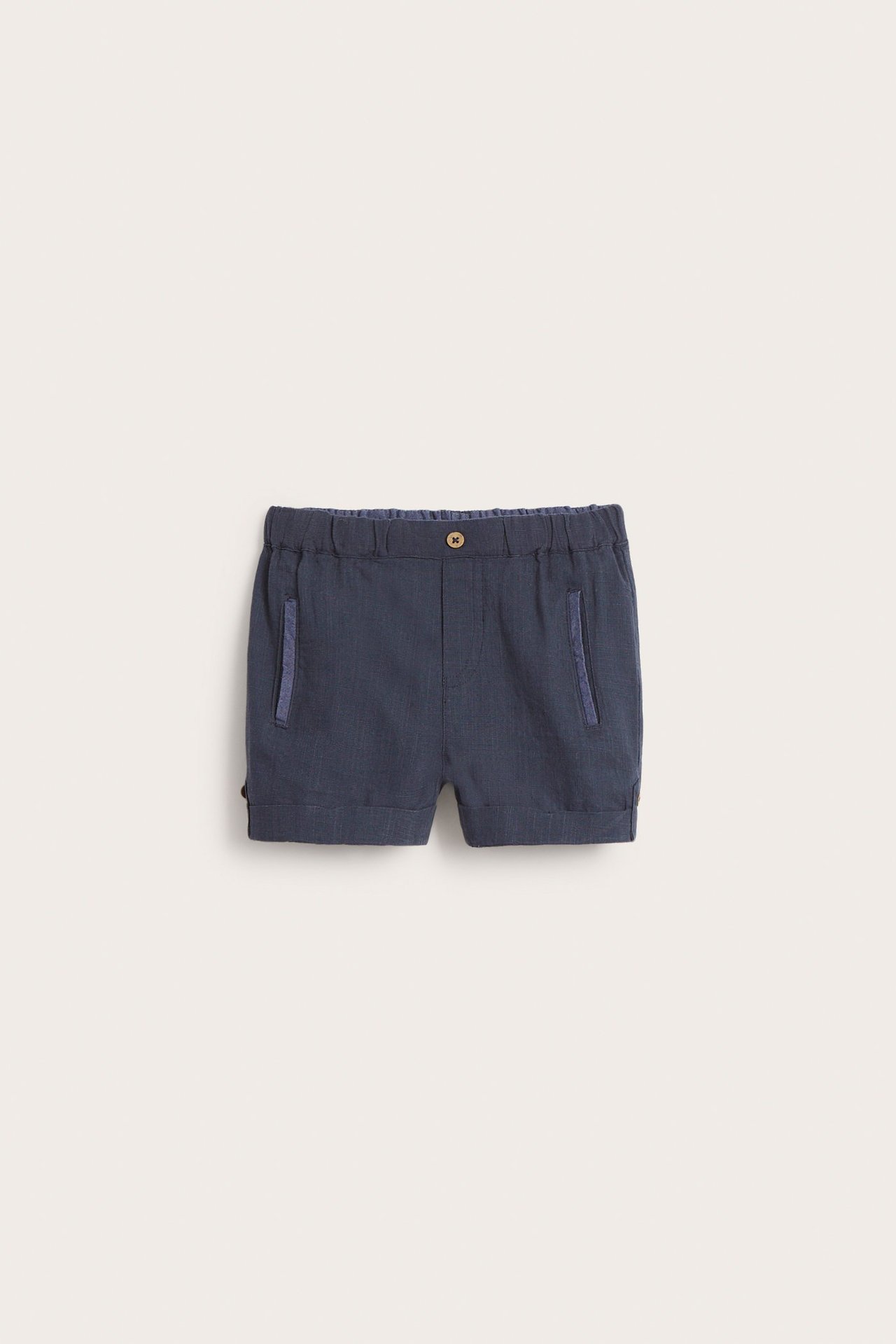 Front view of dark blue woven kid's shorts with elastic waist, front pockets, and decorative coconut buttons.