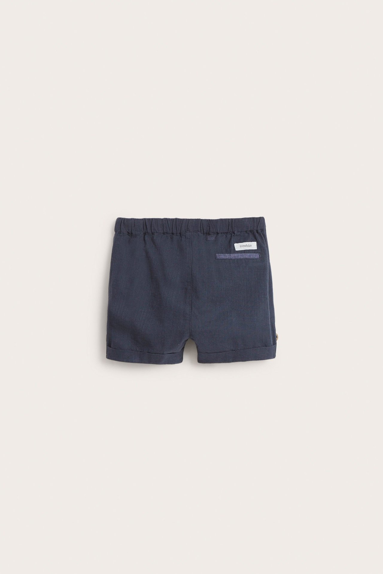 Back view of dark blue woven cotton shorts with elastic waist, decorative back pocket, and rolled hems.