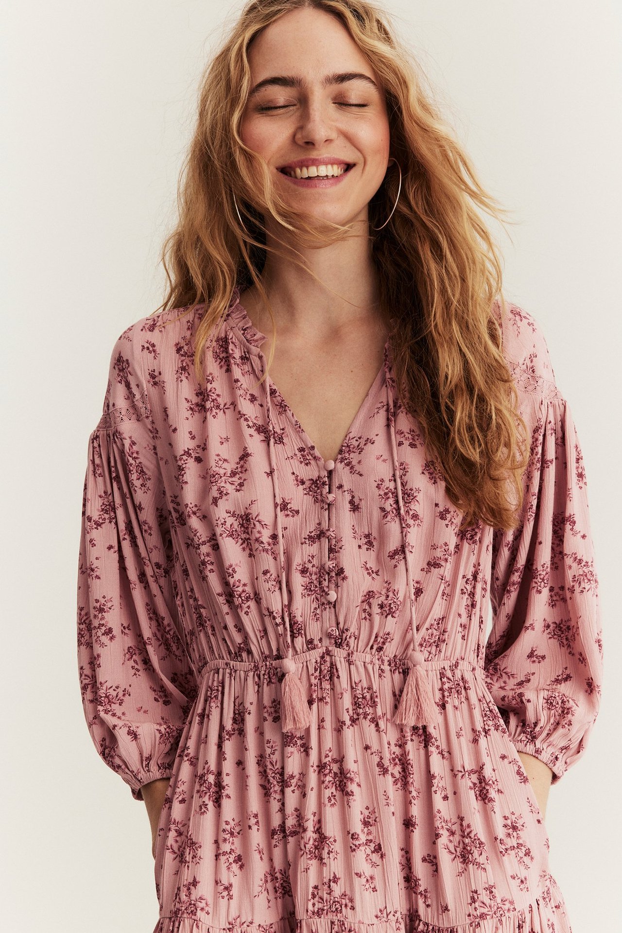 Vorderansicht: Frau in einem rosa geblümten Viskosekleid mit Rüschenkragen, Puffärmeln und Creolen.