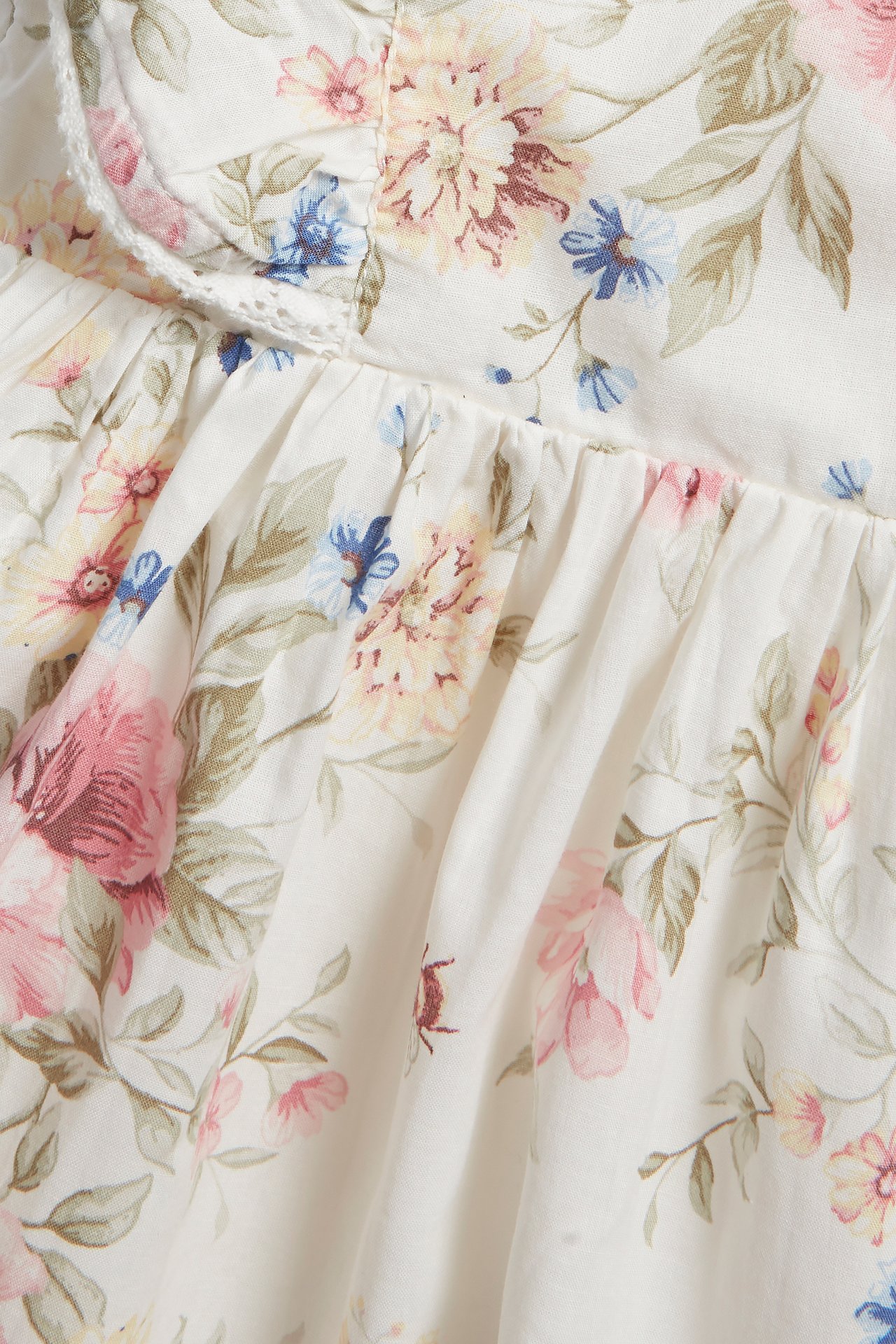 Close-up of an off-white cotton dress with a pink, blue, and yellow floral pattern and lace-trimmed ruffle.