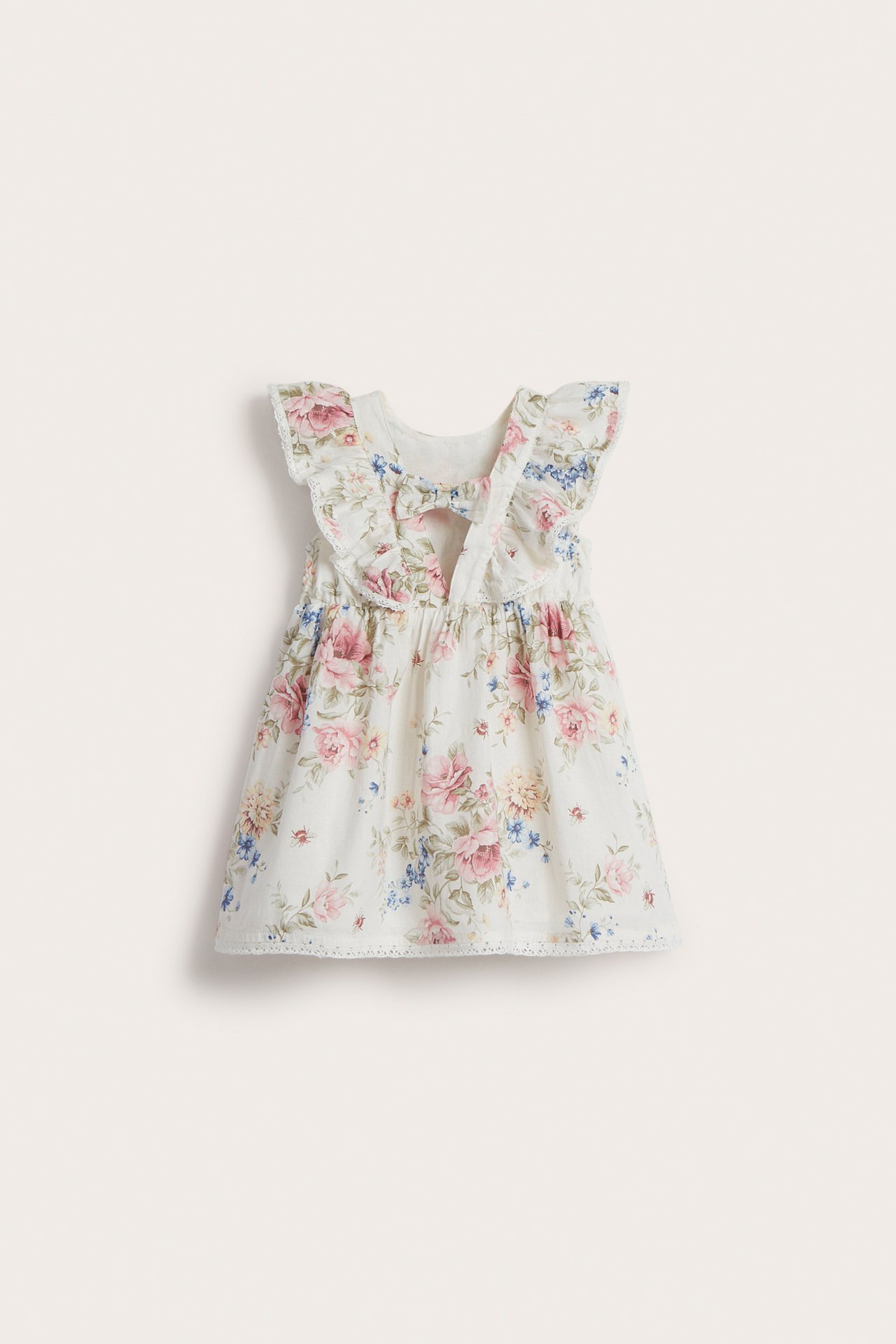 Front view of an off-white kid's floral cotton dress with ruffled sleeves, lace trim, and V-back bow.