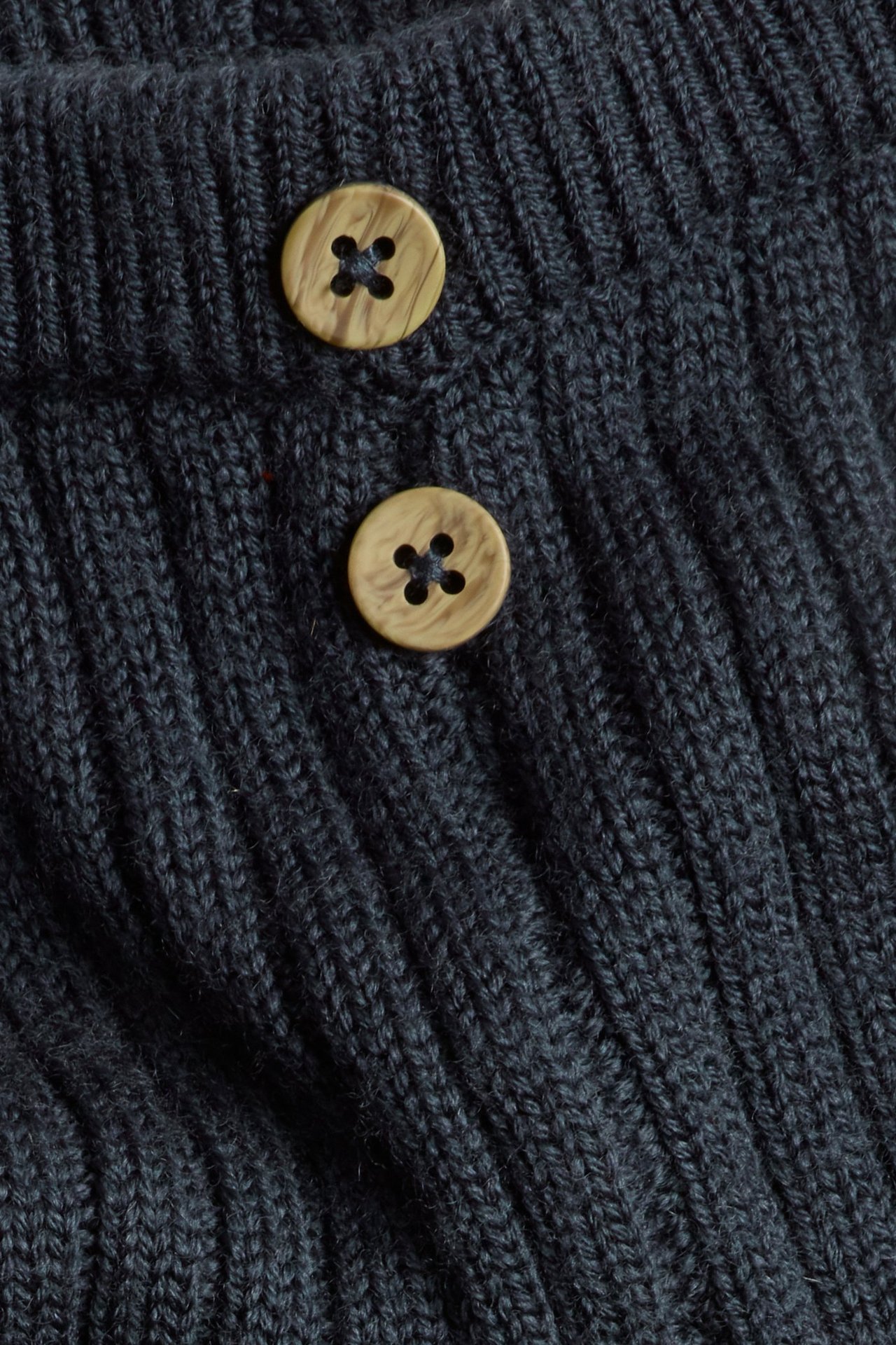 Close-up of dark blue ribbed wool leggings with two decorative light brown wooden buttons.