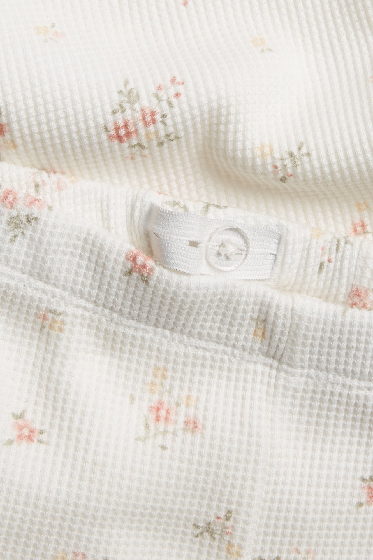 Close-up of off-white floral waffle-knit baby pants with an adjustable elastic waistband and button.