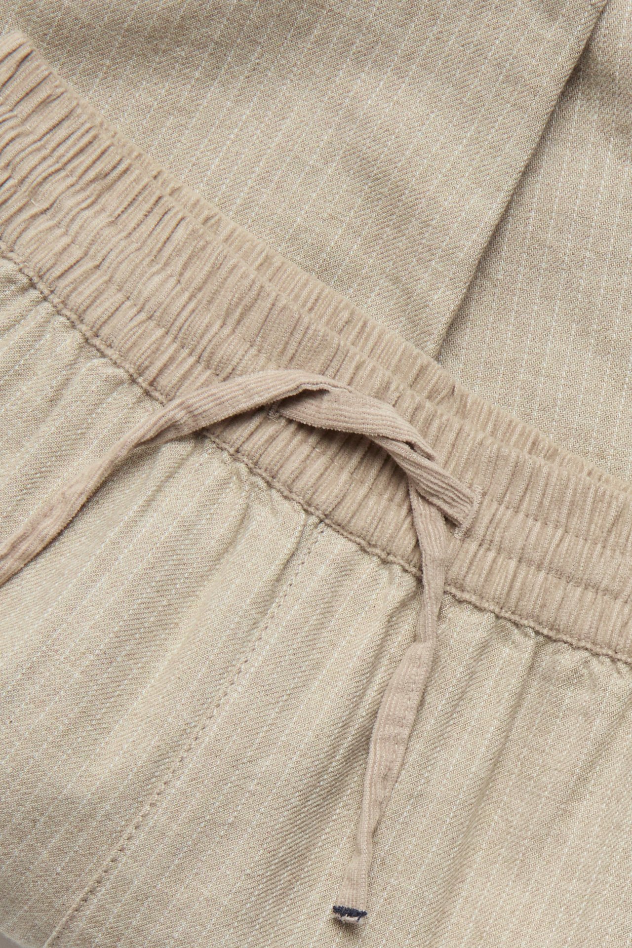 Close-up view of beige melange striped woven pants with an elastic corduroy waistband and drawstring.