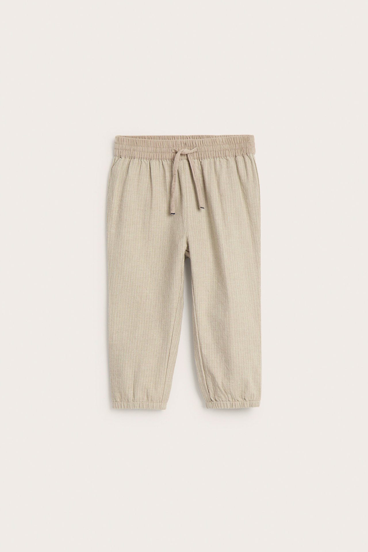 Front view of kid's beige melange striped cotton pants with elastic drawstring waist and elastic cuffs.