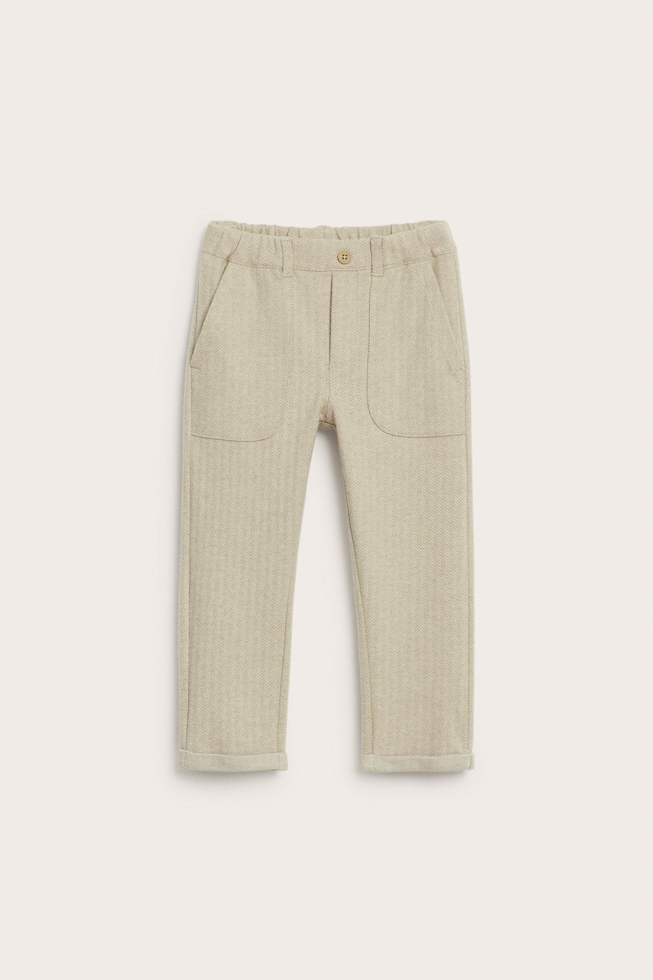 Vorderansicht beigefarbener Melange-Kinderhose mit Fischgrätmuster, Gummizugbund, Zierknopf und hochgekrempelten Bündchen.