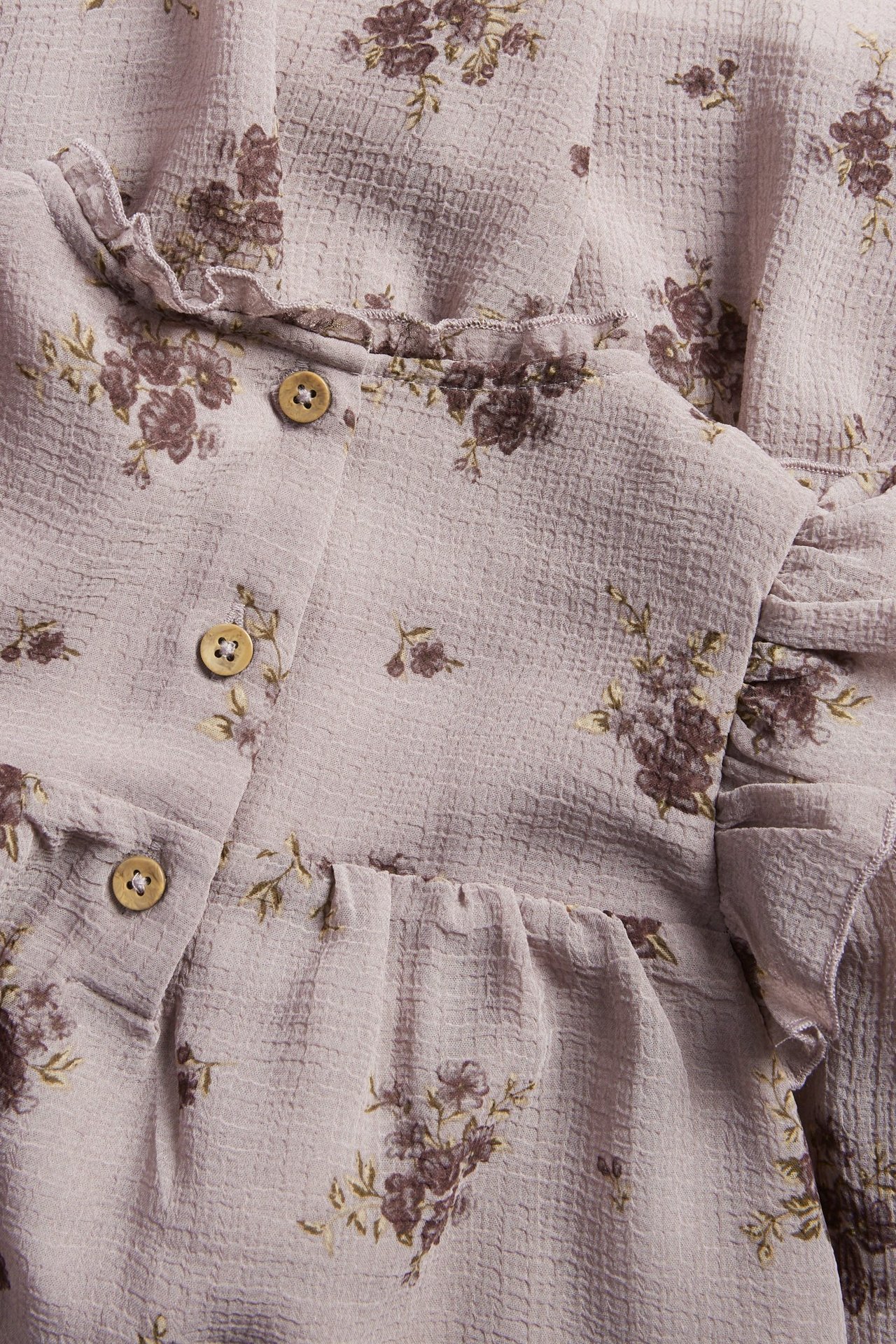 Close-up of a light lilac floral chiffon dress with ruffles and wooden buttons.