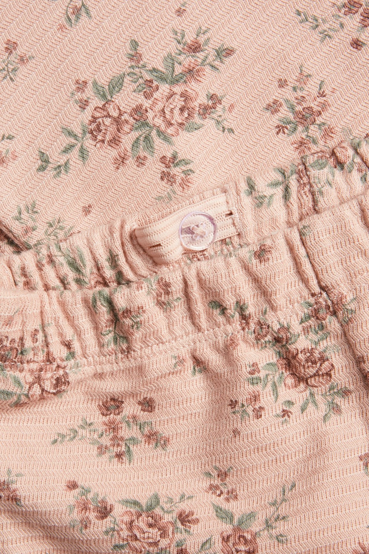 Nahaufnahme von rosa strukturierten Jersey-Leggings mit kleinem Blumendruck und verstellbarem Gummibund mit Knopf.