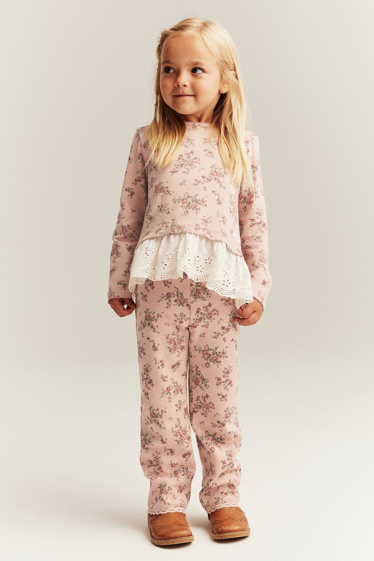 Vorderansicht: Kind in rosa geblümten ausgestellten Leggings mit Spitze, passendem Oberteil und braunen Schuhen.