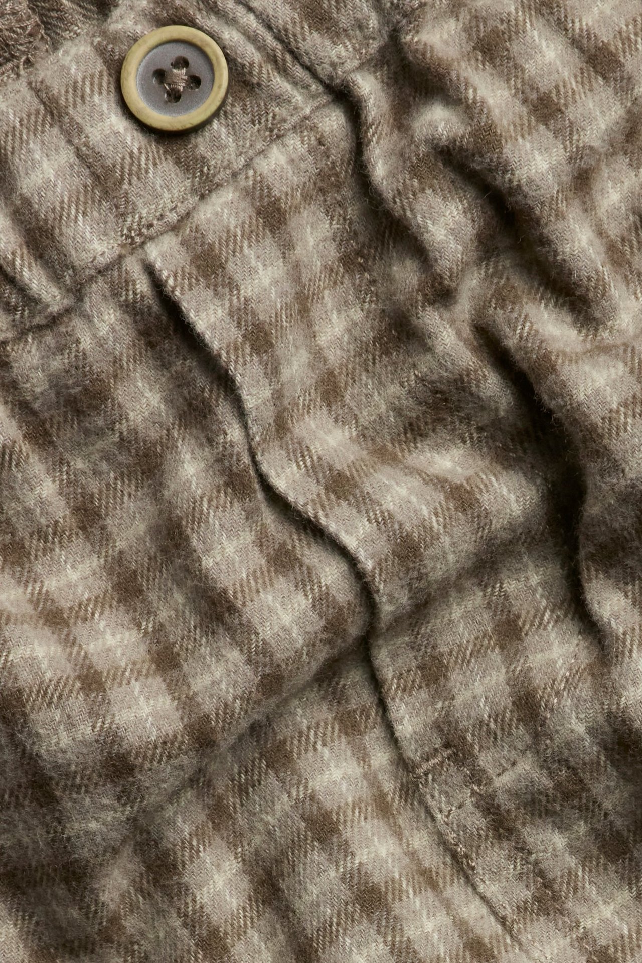 Nahaufnahme einer braunen karierten Twillhose mit einem Zierknopf.